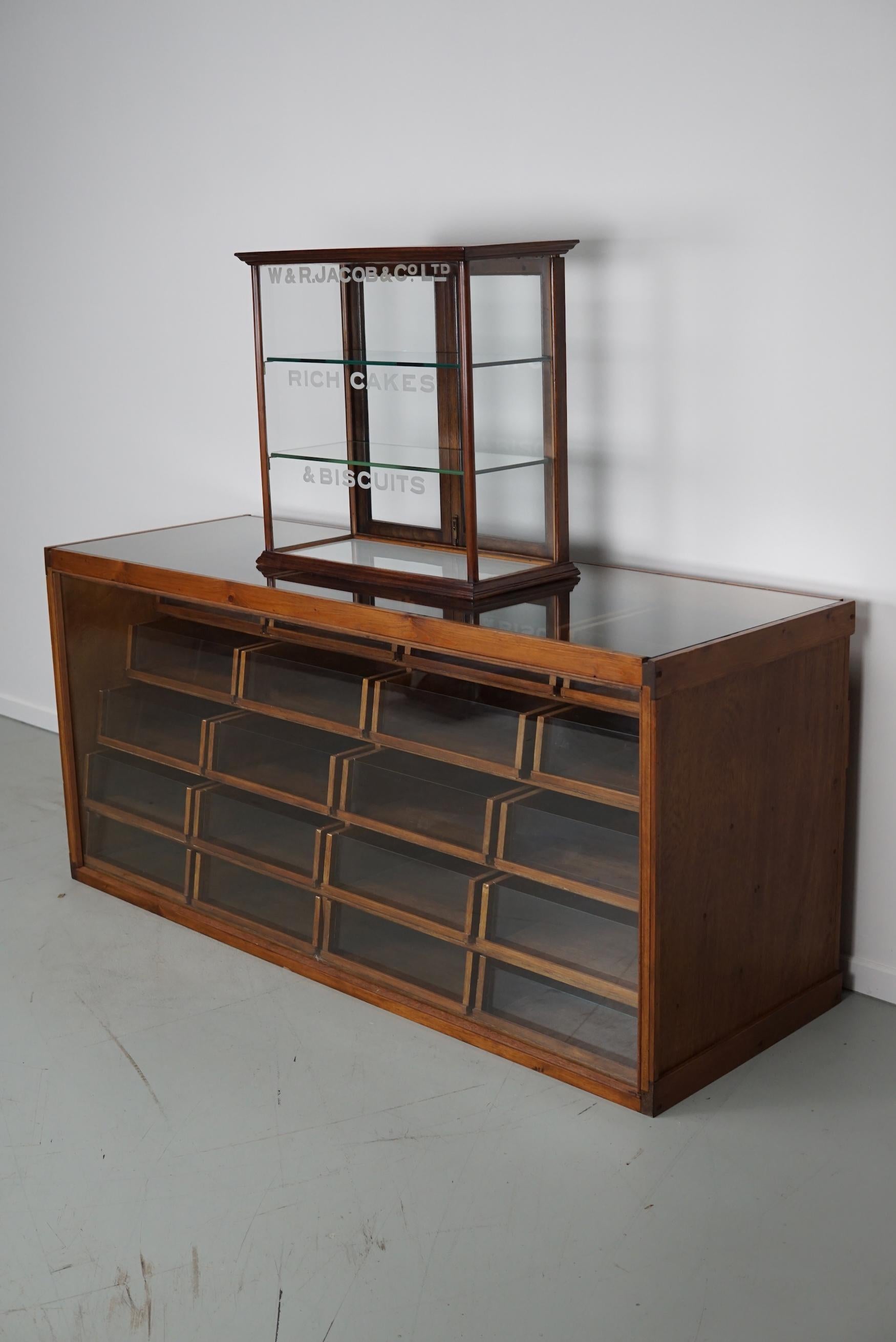 This shop display cabinet was made to display cakes and biscuits. The cabinet has two glass shelves and a white glass bottom. This is a very attractive and useful piece and it is in good antique condition.