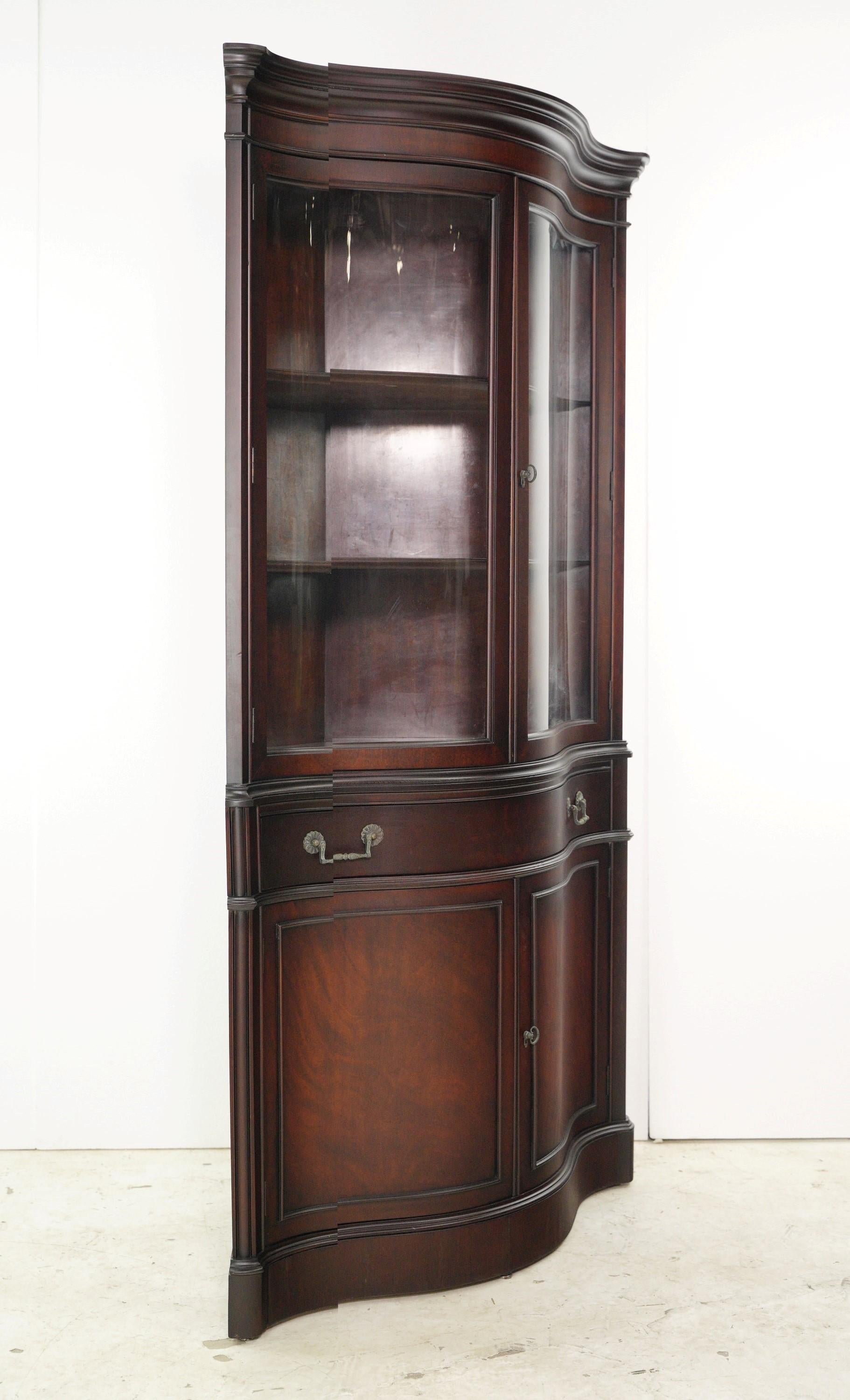 This Traditional curved glass doors corner cabinet is a timeless beauty. Crafted from mahogany, it features elegant curved glass front doors, adding sophistication and showcasing cherished items in a space saving corner design. This also features