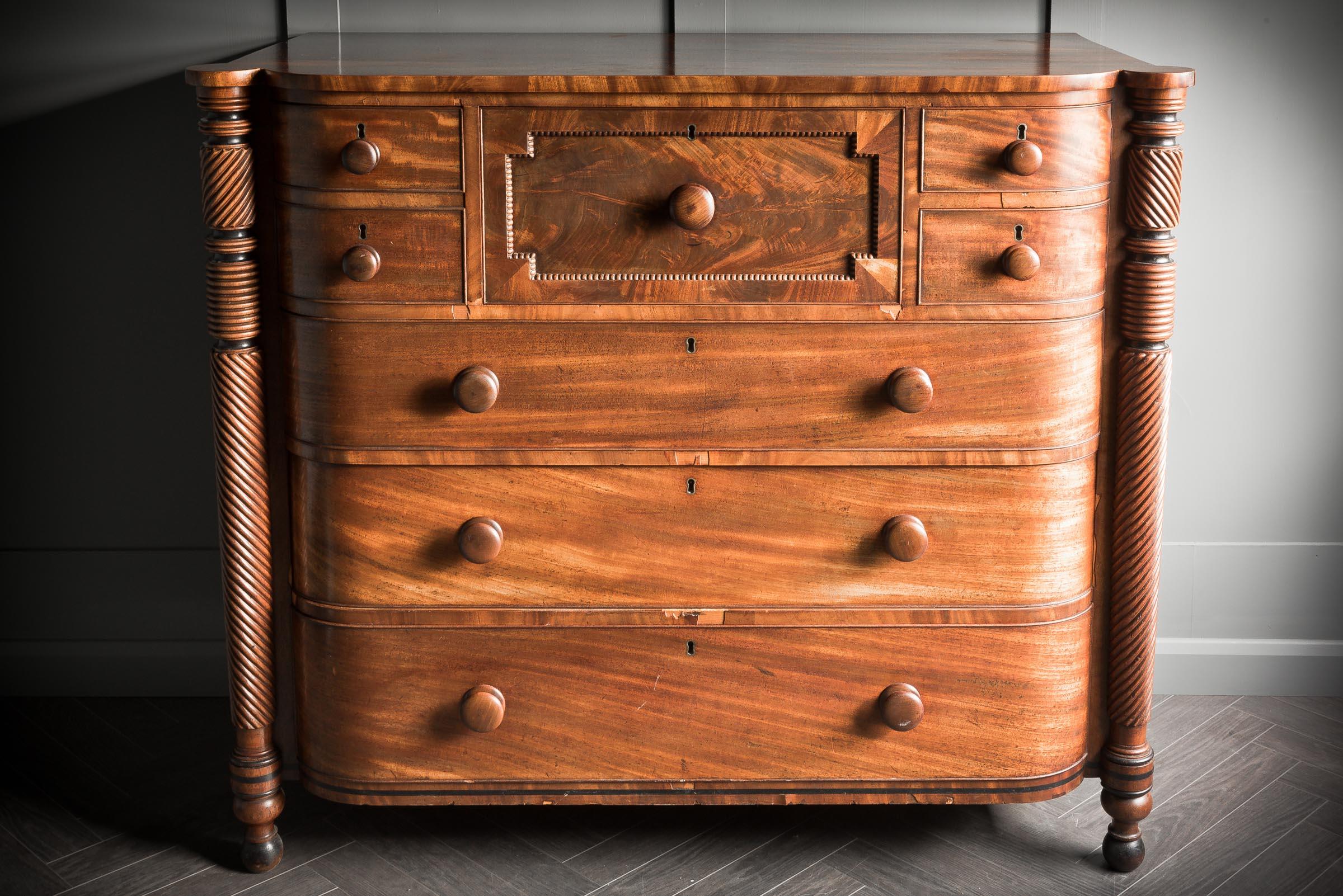 This large Scottish demi bow fronted chest is made from a rich mahogany with intricate carvings on pillars framing the piece. The chest composes of four delicate lockable drawers surrounding the central drawer sitting on top of three bold dressing