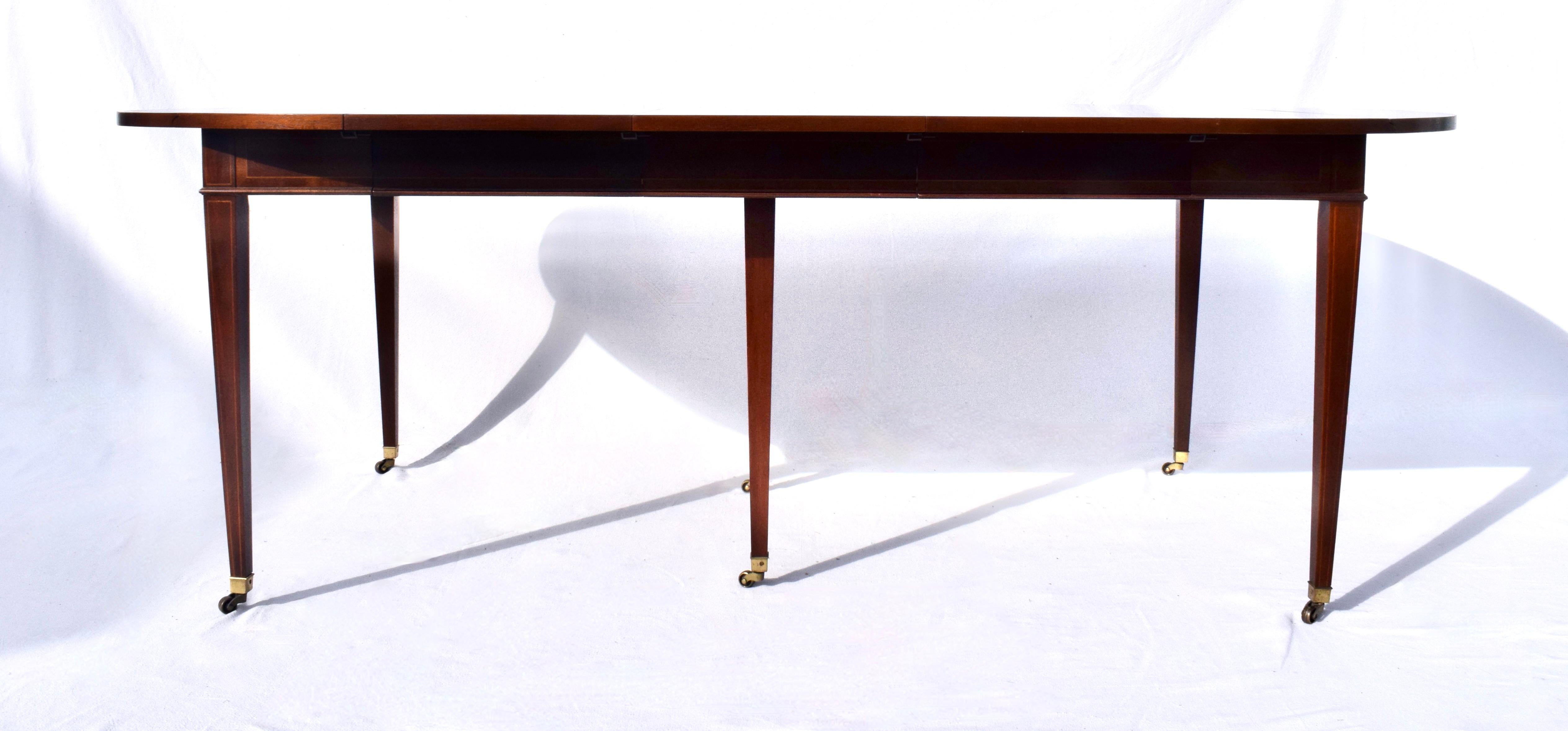 An extraordinary drop Leaf dining table in the late Georgian style with Mahogany banded inlay top and tapered legs on brass casters.  Featuring three 15.5