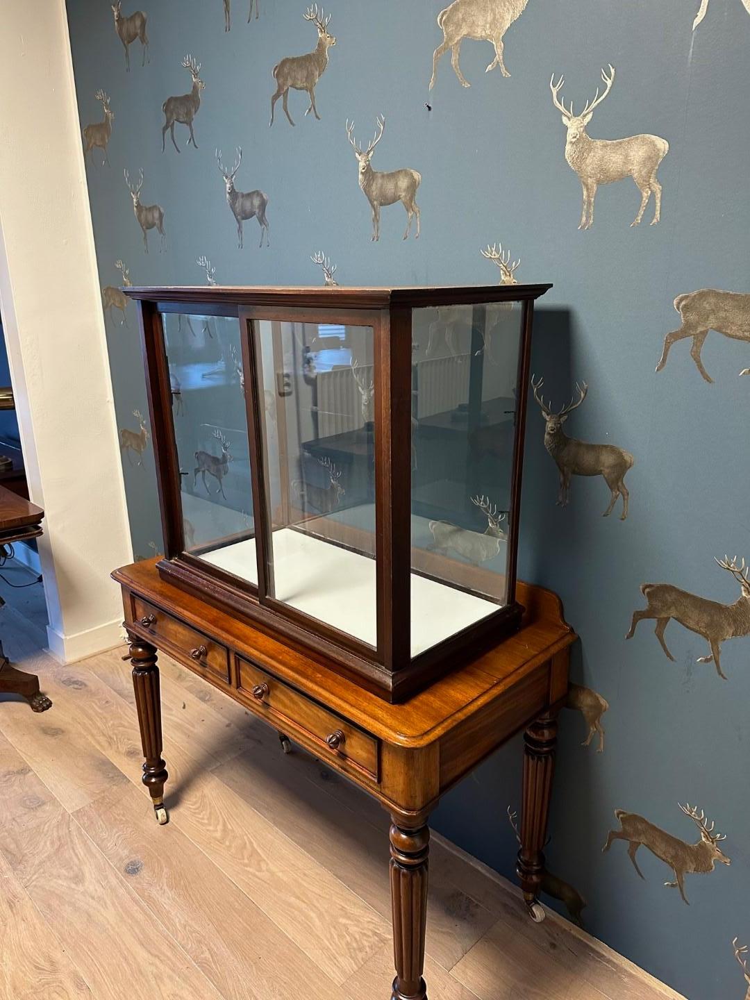 Antique mahogany display case in good and original condition. The display case has 2 sliding doors. There are supports for an extra glass shelf. Extra shelf is not included. The table on which the display case stands is not part of the display