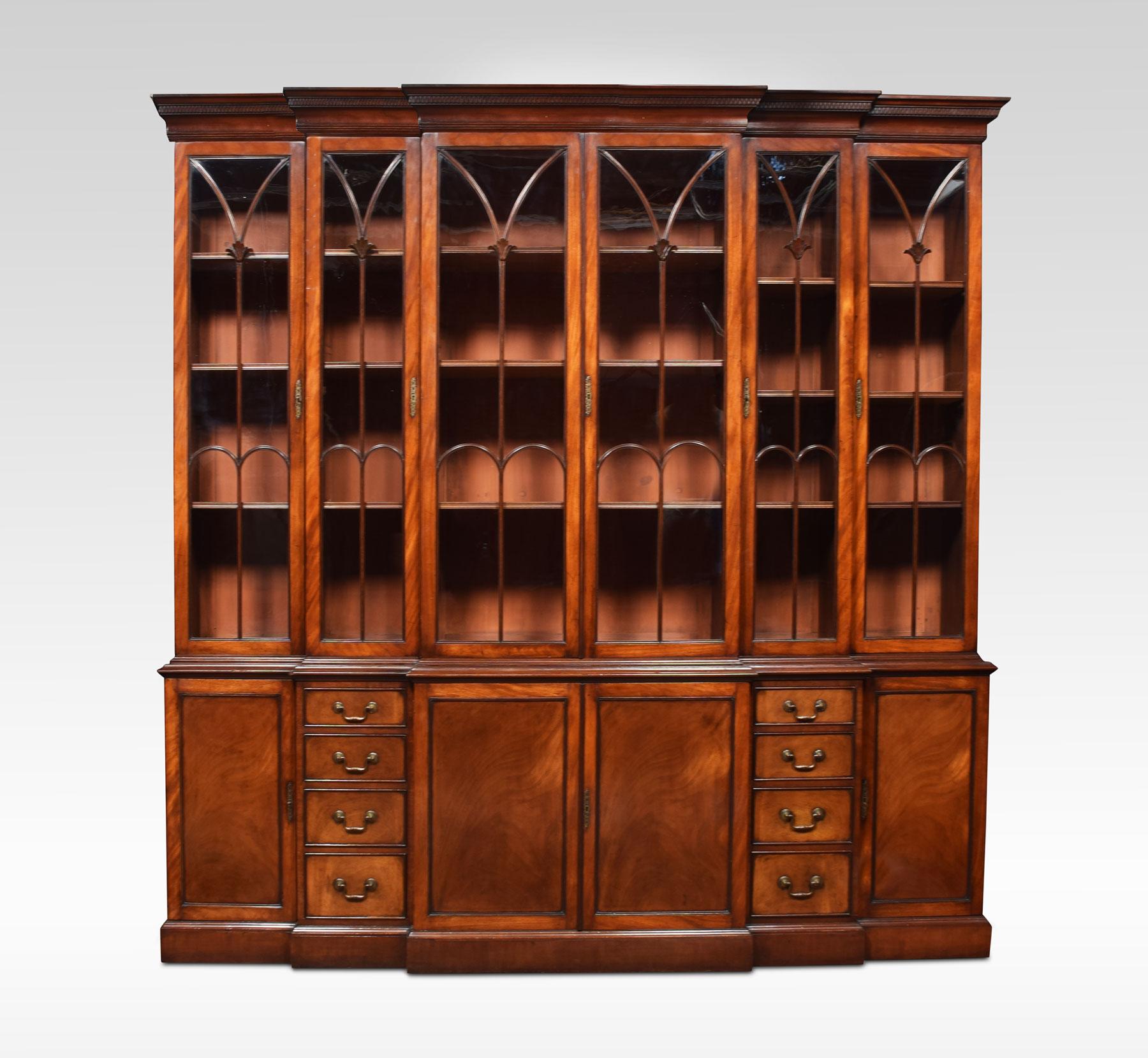 George III style mahogany breakfront bookcase. The molded cornice with carved frieze over two central cupboard doors with arched beaded glass, with stylized floral decoration. Flanked on each side by narrow cupboards and a wider cupboard, fitted