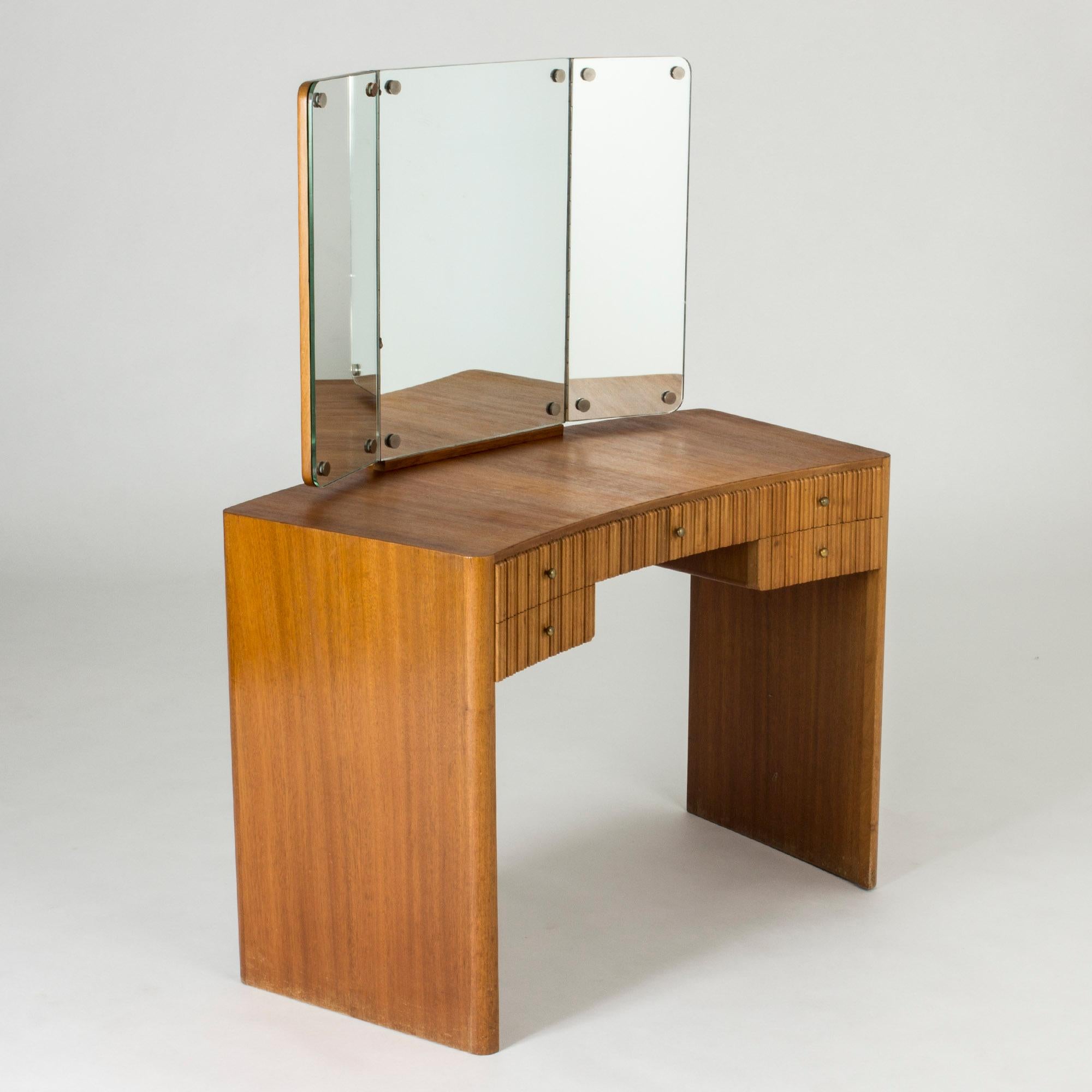 Beautiful mahogany dressing table by Carl-Axel Acking, with clean rounded lines. Mirror in three sections with adjustable sides. Striking “corrugated” look of the wood on the drawer fronts, neat brass knobs.