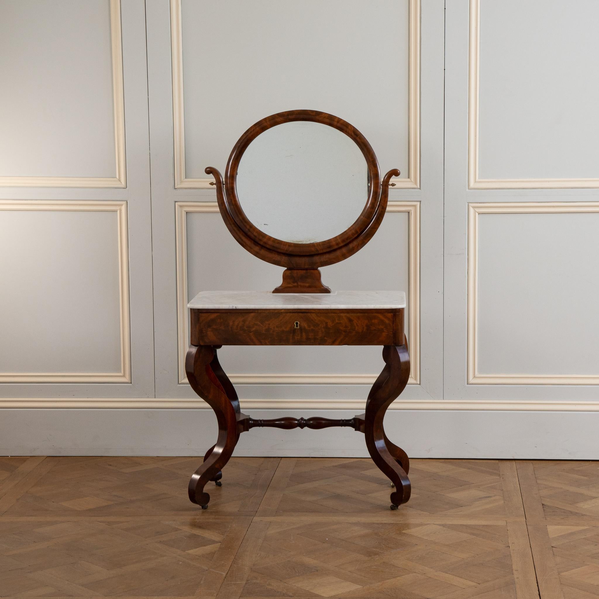 Une très élégante coiffeuse française en acajou de la période de restauration (début du 19ème siècle).
Assis sur 4 pieds galbés 
 a un dessus en marbre avec un miroir de Psyché.
le tiroir a un dessus en cuir qui était utilisé comme table