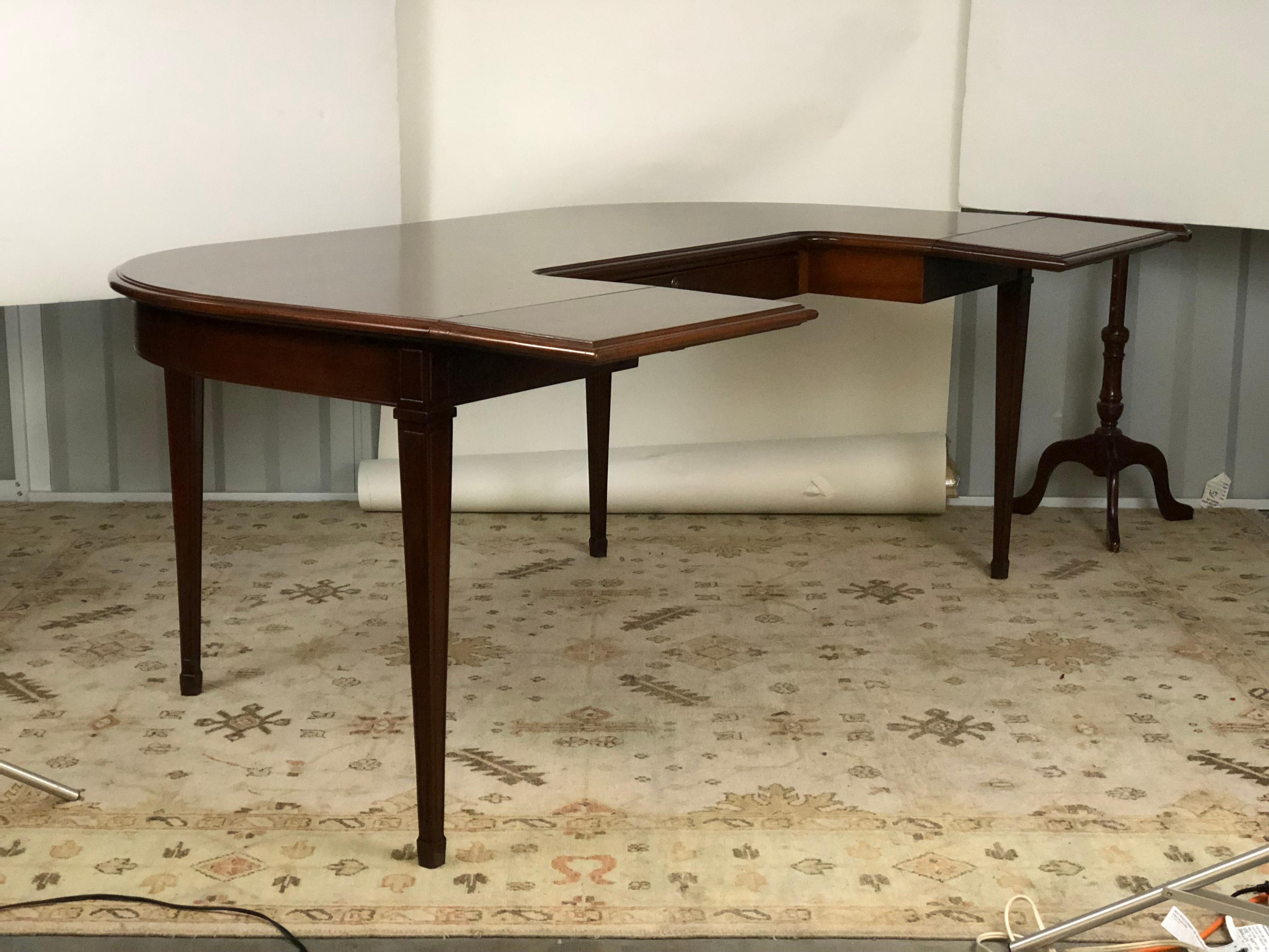 20th century American mahogany demilune shaped desk or writing table with drop-leaf extensions flanking a fitted drawer in the frieze. The table is raised on tapered legs and spade feet. The desk opens to 46.25 inches deep when the leaves are fully