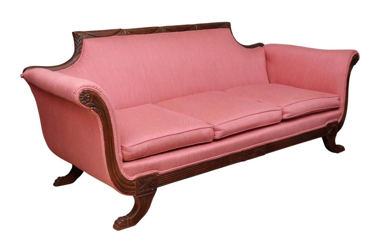 An American classical style Duncan Phyfe three seat sofa. Carved throughout with swag details on the flat crest rail, rosettes in front of rolled arms and reeded lines on the apron. Stands on reeded legs carved with shell feet. Upholstered in a pink