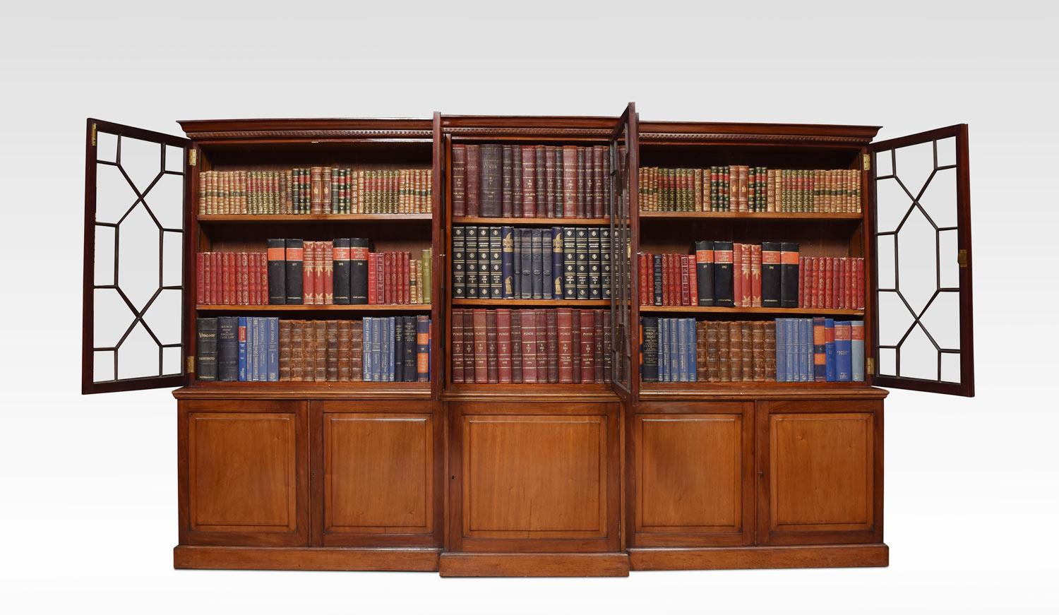 George III style mahogany library bookcase, the moulded dentil breakfront cornice above five astragal glazed doors enclosing adjustable shelved interior. To the base section having five panelled cupboard doors all raised up on plinth
