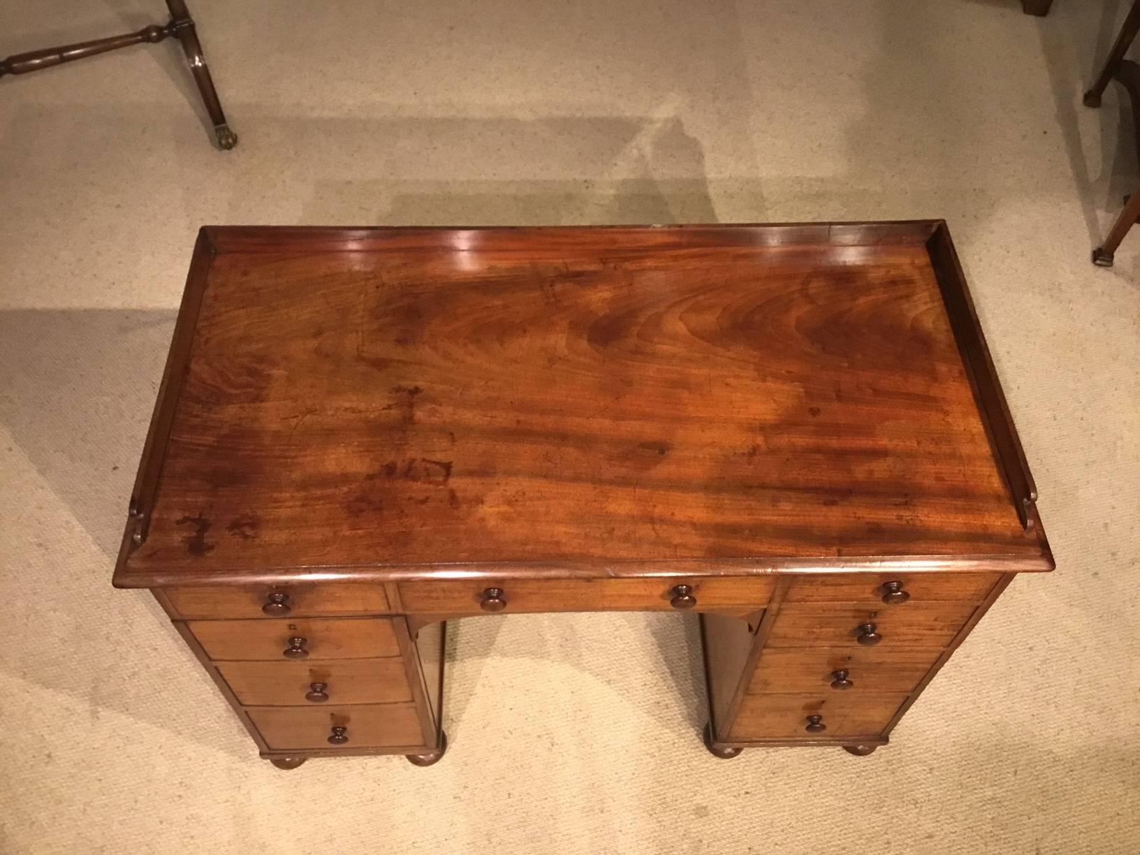 A mahogany early Victorian period writing desk. Having a solid figured mahogany rectangular top with a raised gallery and a moulded edge. With an arrangement of six mahogany lined drawers with one rectangular cupboard with 