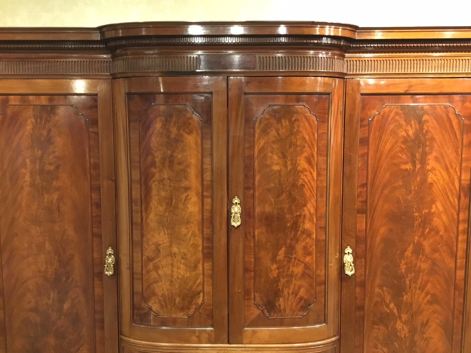 A mahogany Edwardian period breakfront wardrobe by Howard & Sons of London. The cornice having dentil moulding and an arcaded frieze above an arrangement of four panelled doors and six rectangular drawers veneered in mahogany with oak and cedar