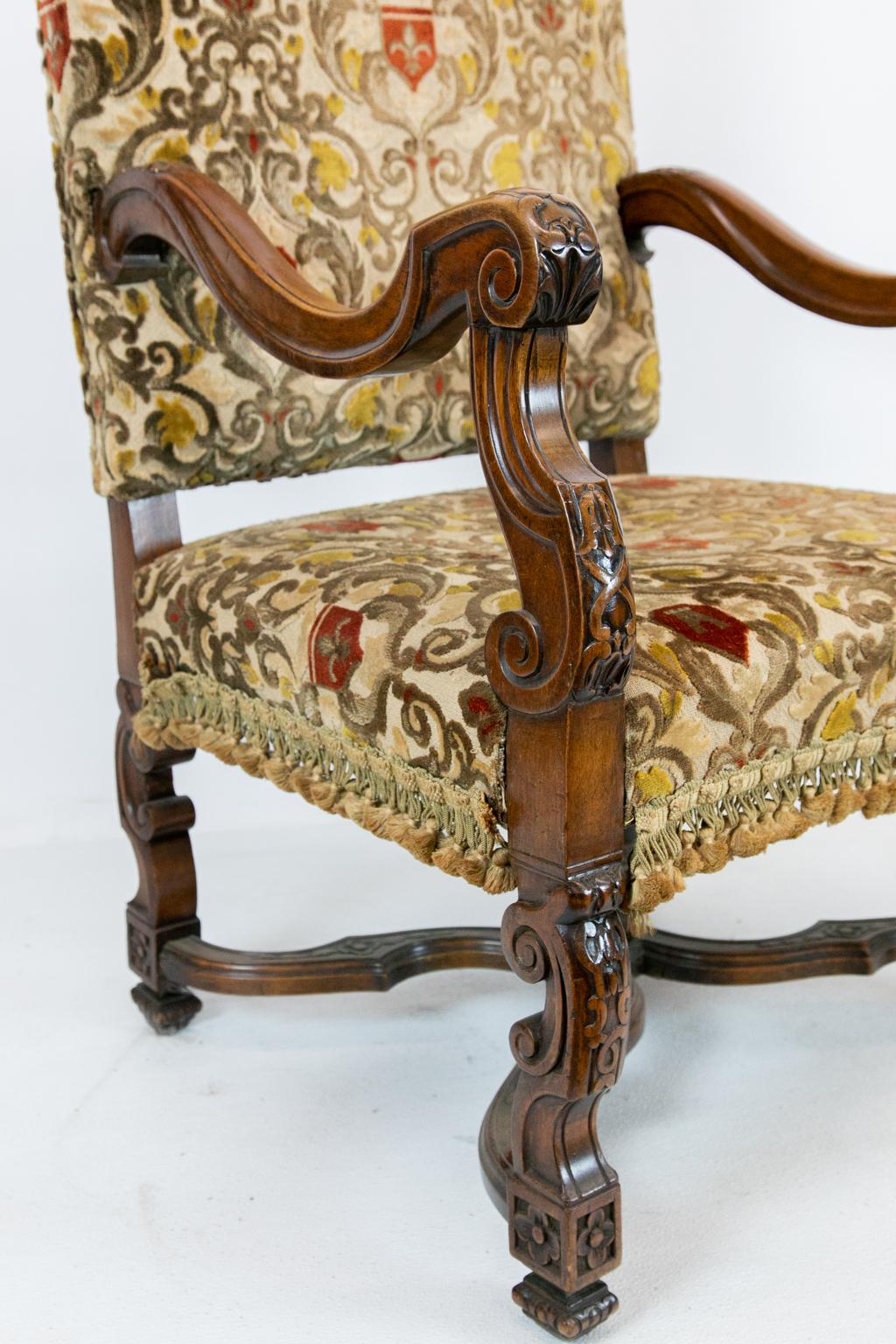 Mahogany English carved walnut upholstered crewel work armchair is carved with acanthus leaf and has shaped sides with bellflower and interlaced ribbon. It has a molded shaped cross stretcher with a carved flower finial. The crewel work extends to