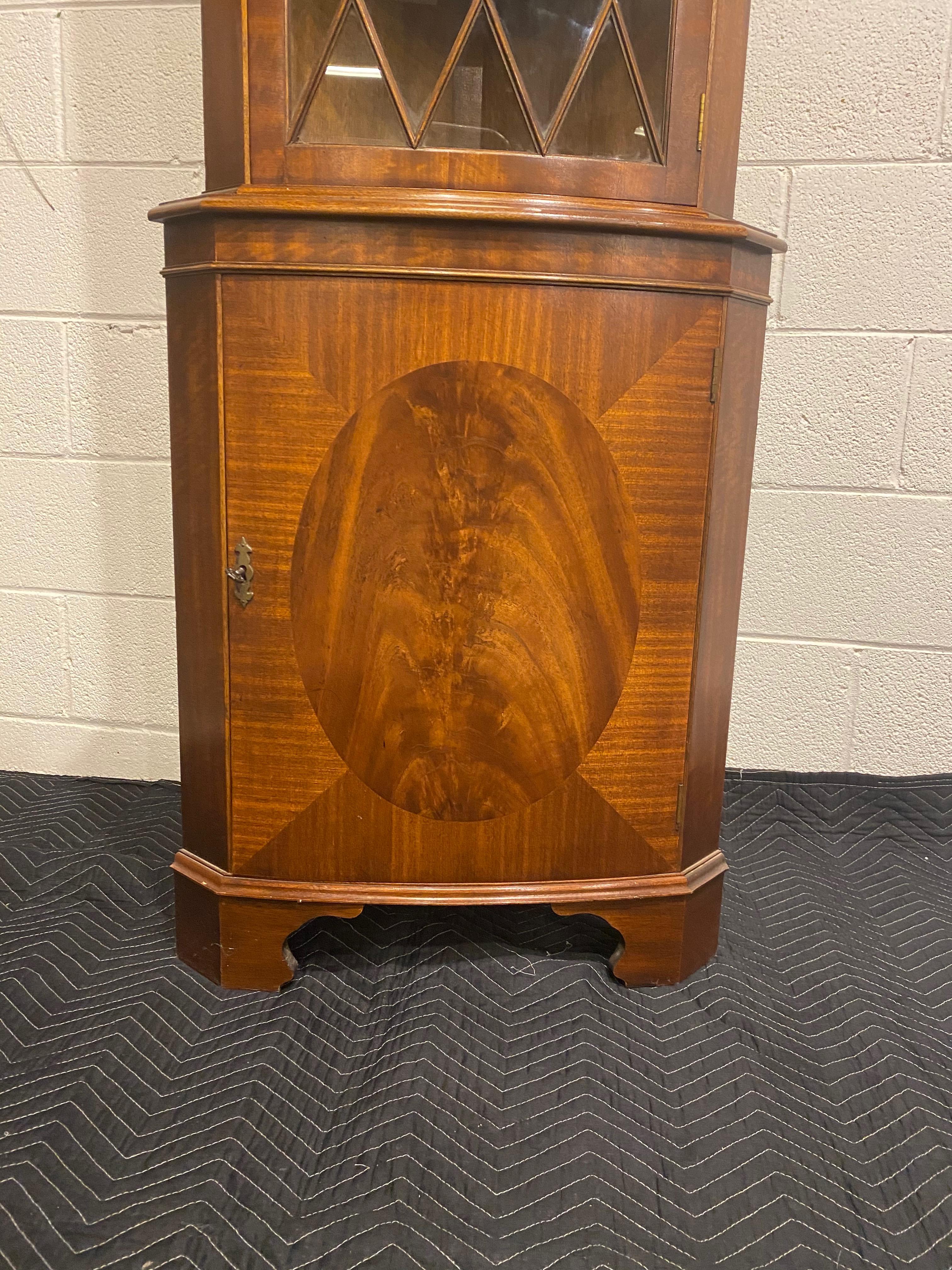 A lovely mahogany corner cabinet with a bowed shape curved front face, glass door with individual hand glazed panes. Single door top and bottom, bottom door is a figured mahogany centre panel with a mahogany cross band detail. Dentil moulding on the