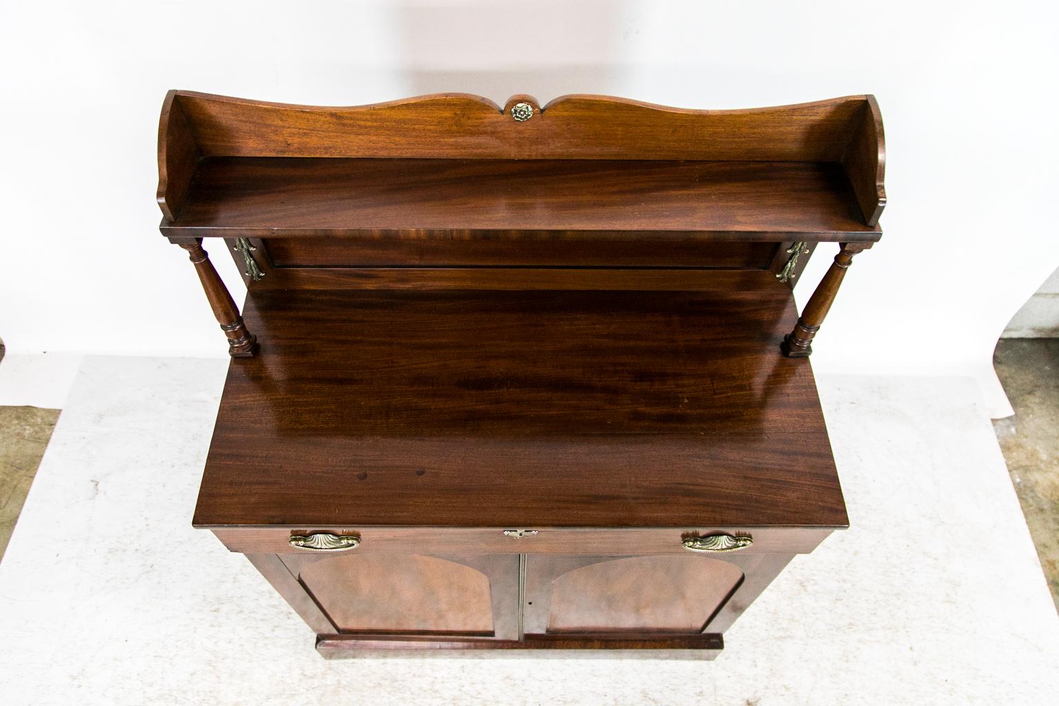 This buffet/server has a rear gallery with a shaped crest. There is a five-inch-deep shelf supported by turned columns. The back has a recessed panel. There is a drawer above two lower doors that have recessed arched panels and the original reeded