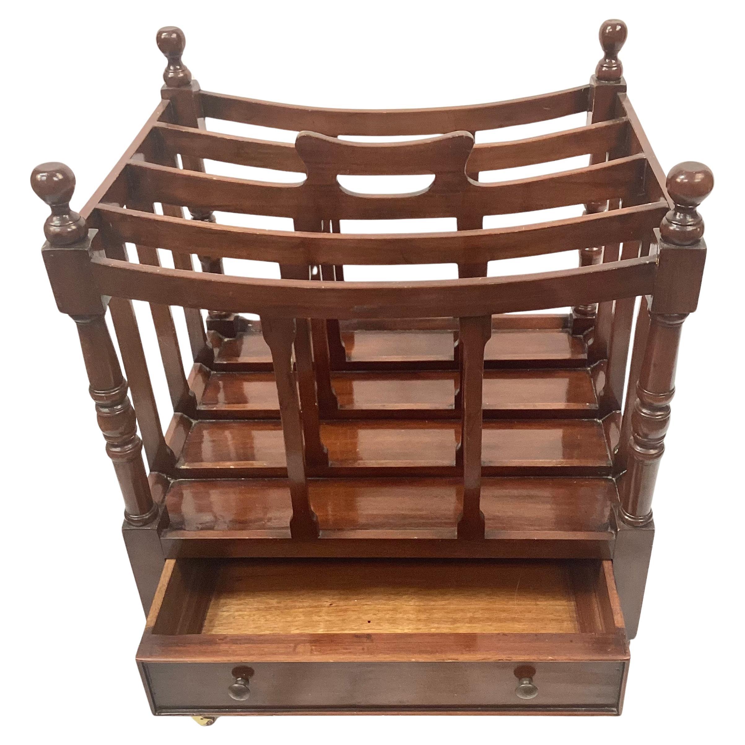 Portariviste Canterbury inglese in mogano del XIX secolo con rotelle in ottone.  Presenta quattro divisori curvi e un unico cassetto in legno. La rastrelliera poggia su gambe affusolate che terminano con rotelle in ottone. 