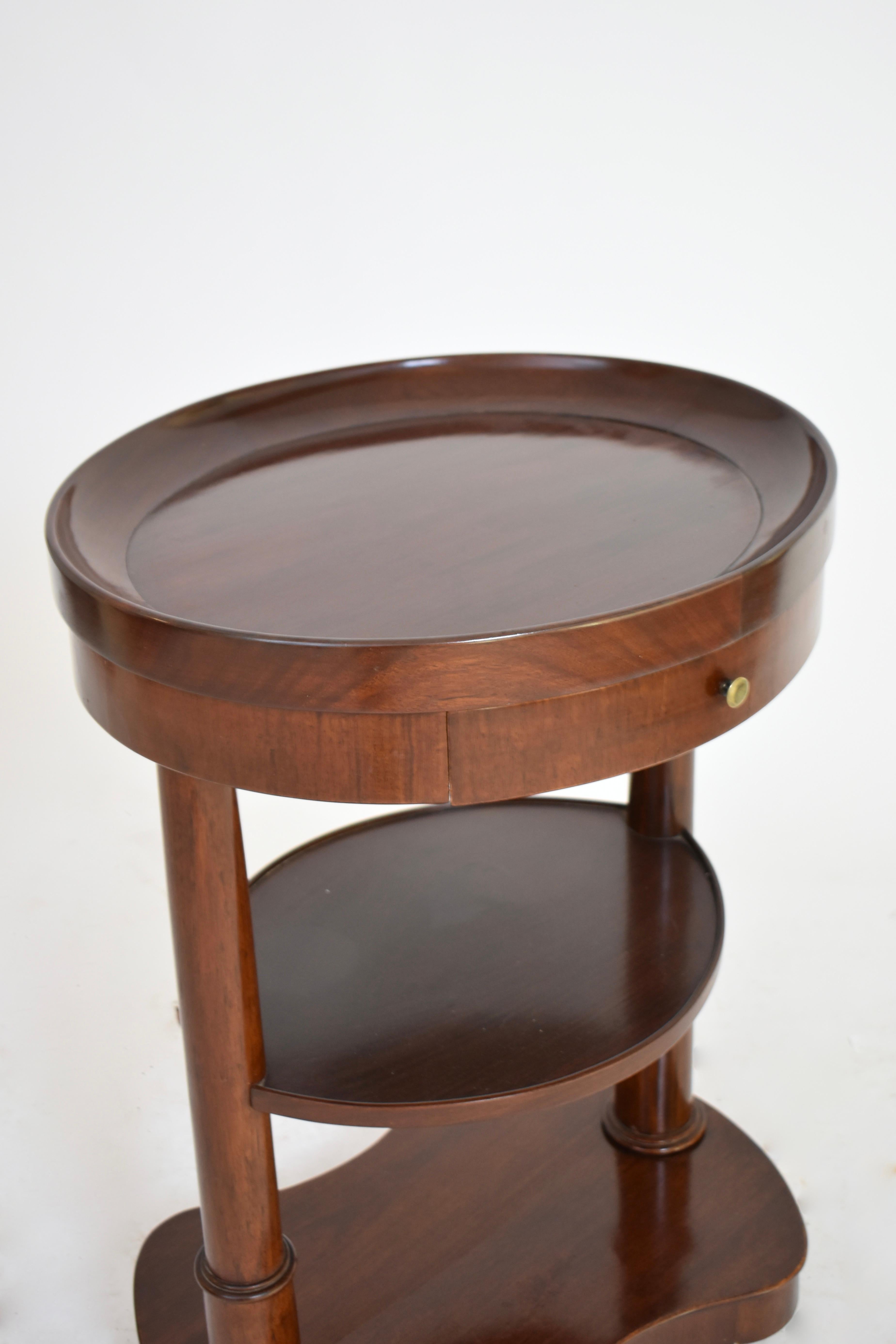 A mahogany and mahogany veneer oval flying table with a basin top, a belt drawer, and column uprights joined by a kshelf. It rests on a curved kidney shape base with casters. France, 19th c.