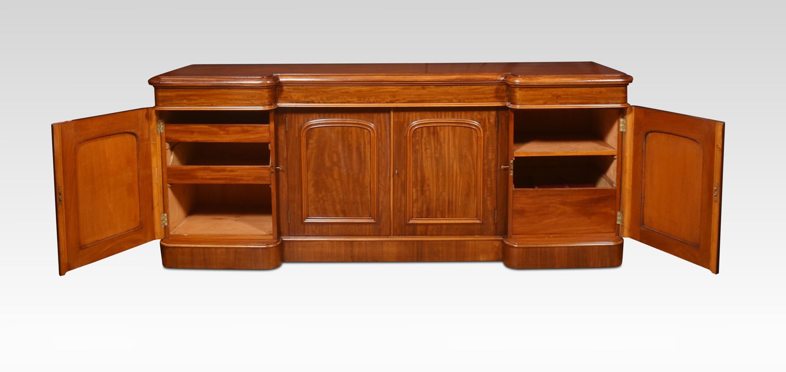 Four-door sideboard, the large rectangular mahogany top with moulded edge and three frieze drawers. Above a pair of recessed, arched and panelled figured mahogany cupboard doors. enclosing a shelf, flanked by further arched and panelled doors