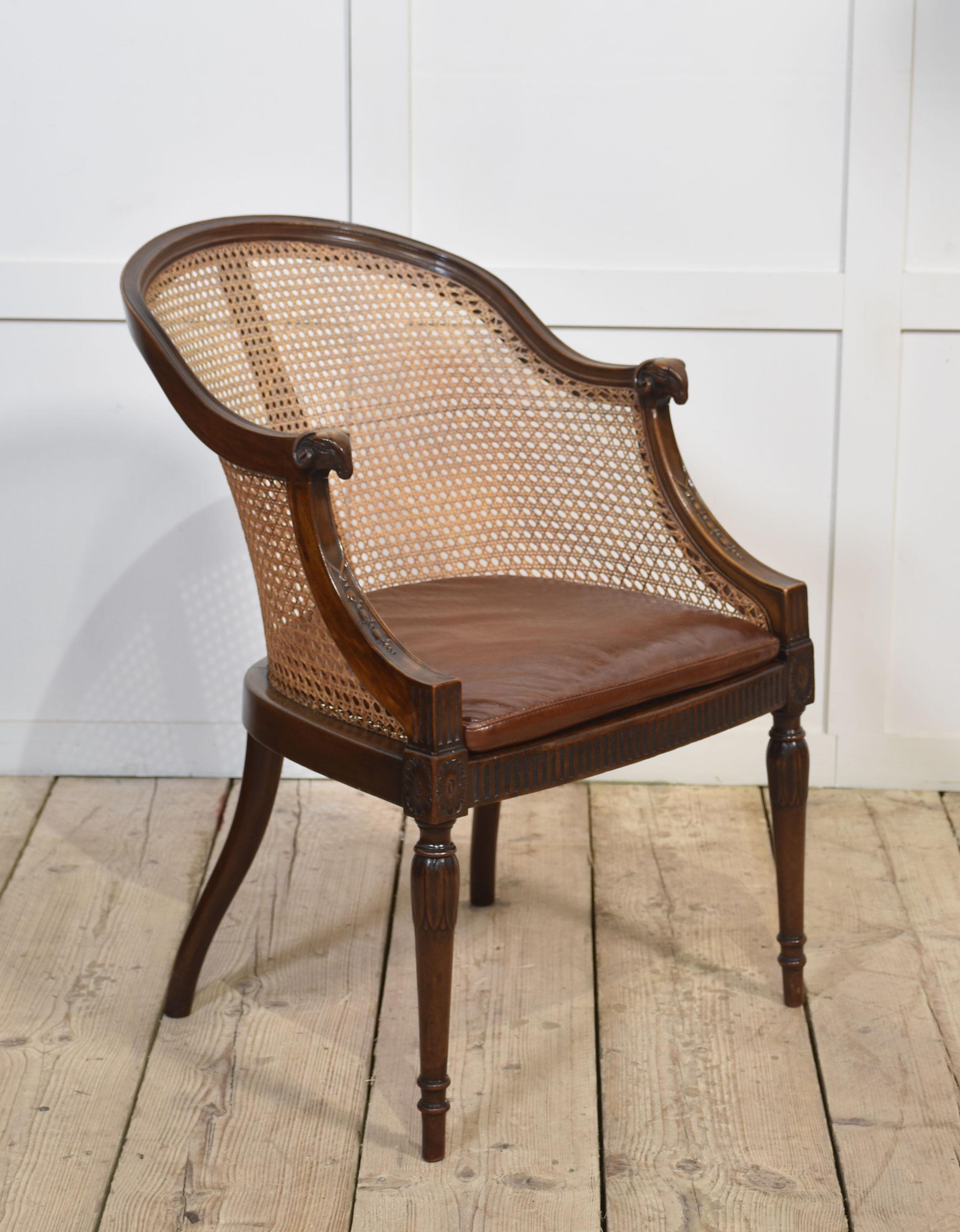 Sillón de bañera con armazón de caoba, los travesaños superiores perfilados con terminales de cabeza de carnero encierran respaldo y asiento de bergere con cojines extraíbles. Todo ello se eleva sobre patas torneadas, ahusadas y