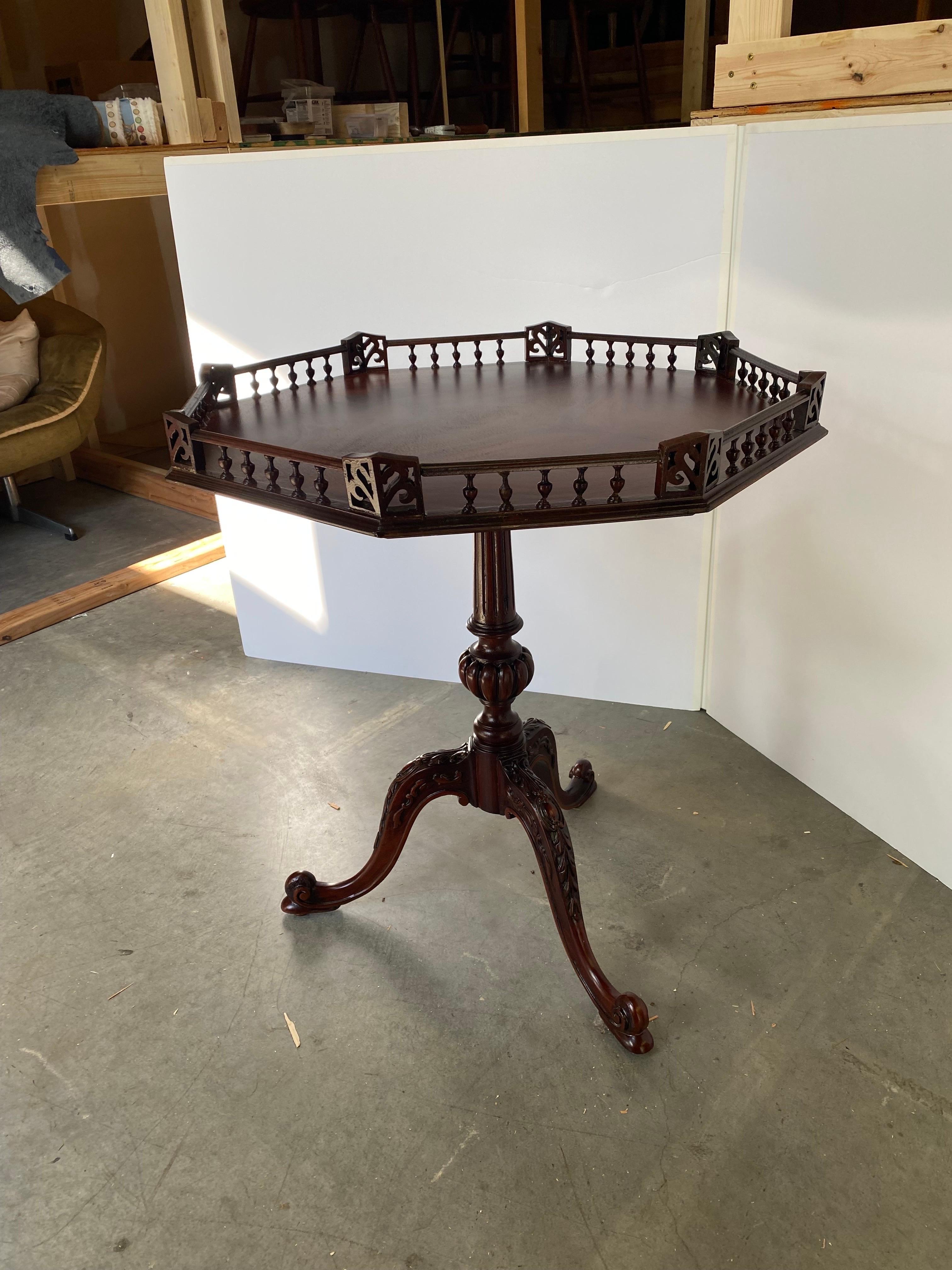 A flame mahogany gallery edge Chippendale style tea table.  The octagonal top, with balustrade gallery railing supported by a center column with pumpkin form carving supported by three hand carved cabriole legs.  The finish has been professionally
