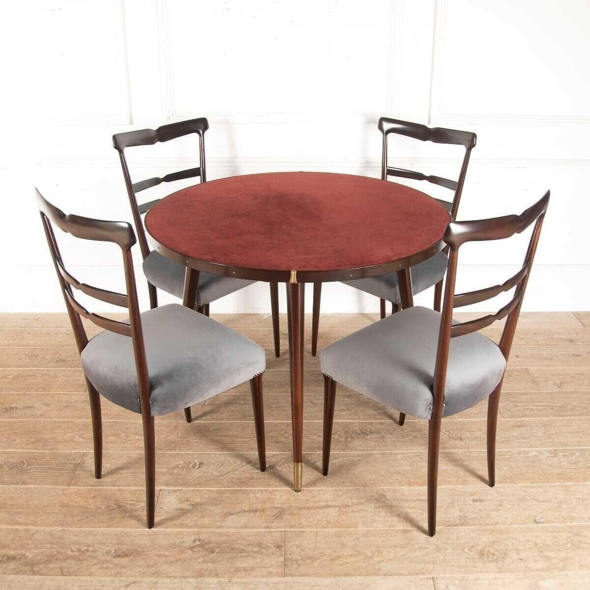 Smart circular games or breakfast table, in dark tinted mahogany. With four elegant high-backed dining chairs, which have been reupholstered in grey velvet. 
This table, with a dark glass top over an original brick red suede surface. Four swing-out