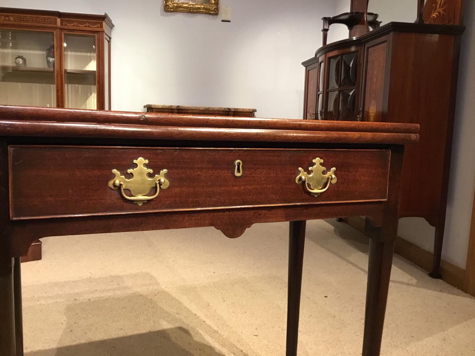 A mahogany George II Period fold over tea table. Having a rectangular Cuban mahogany top with re-entrant corners which opens to reveal a mahogany interior. The front with an oak lined drawer with the original brass handles and supported on circular