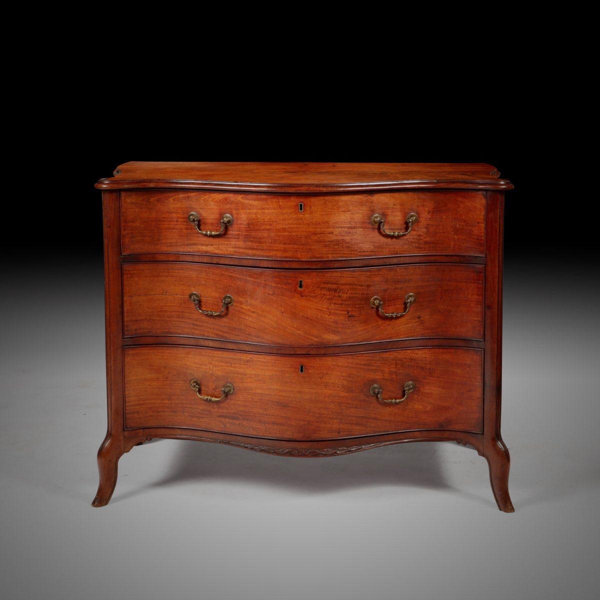A fine George III mahogany serpentine commode, England, circa 1770. Attributed to Henry Hill, Marlbrough.

The three graduated drawers retain their original gilt brass handles over a unique carved apron and flanked by moulded angles continuing