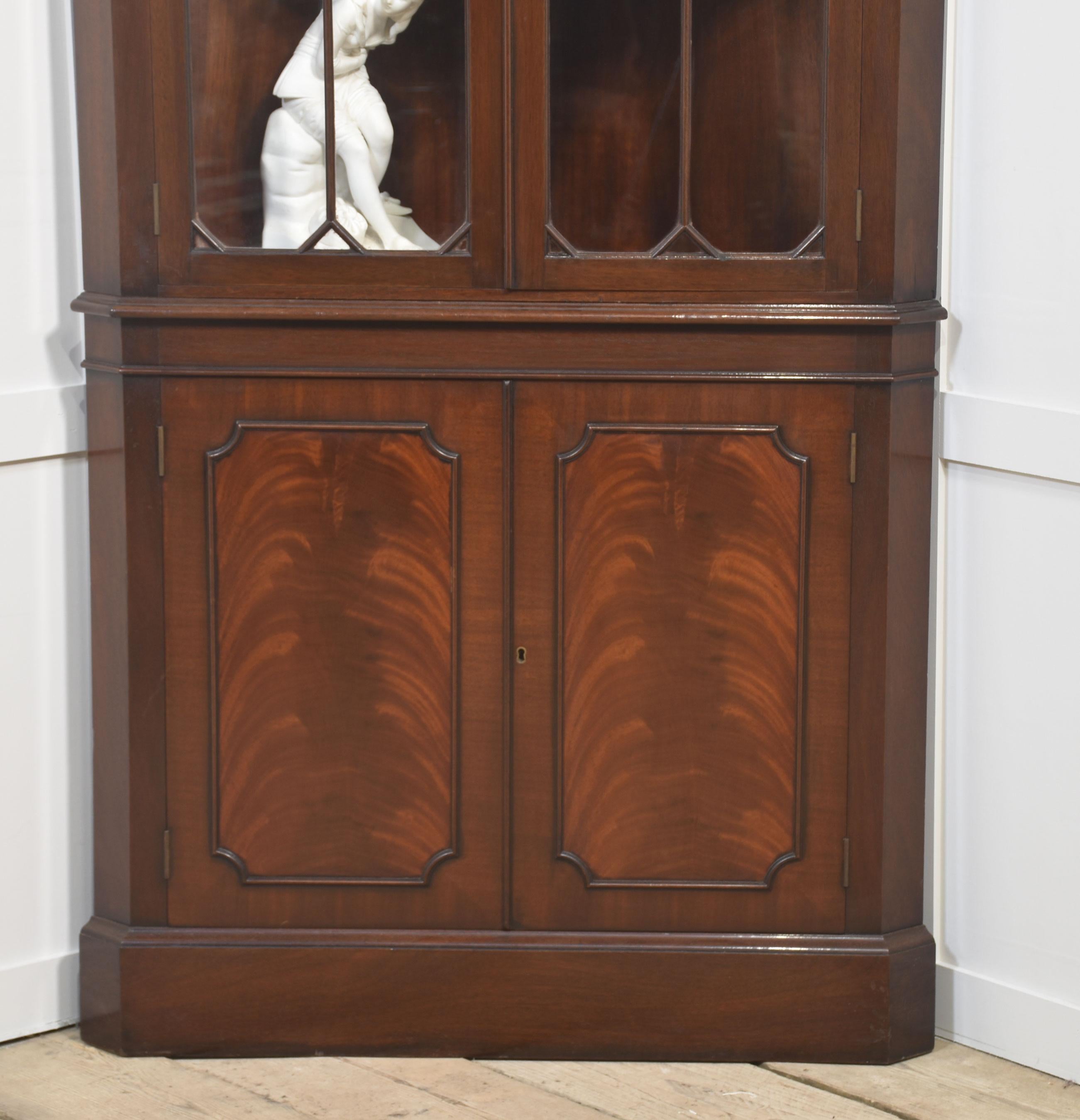 Armario esquinero de pie, de caoba, con la parte superior moldurada sobre un par de puertas acristaladas con reborde que se abren para revelar un interior con estantes. La base está provista de un par de puertas de paneles de caoba bien labrados que