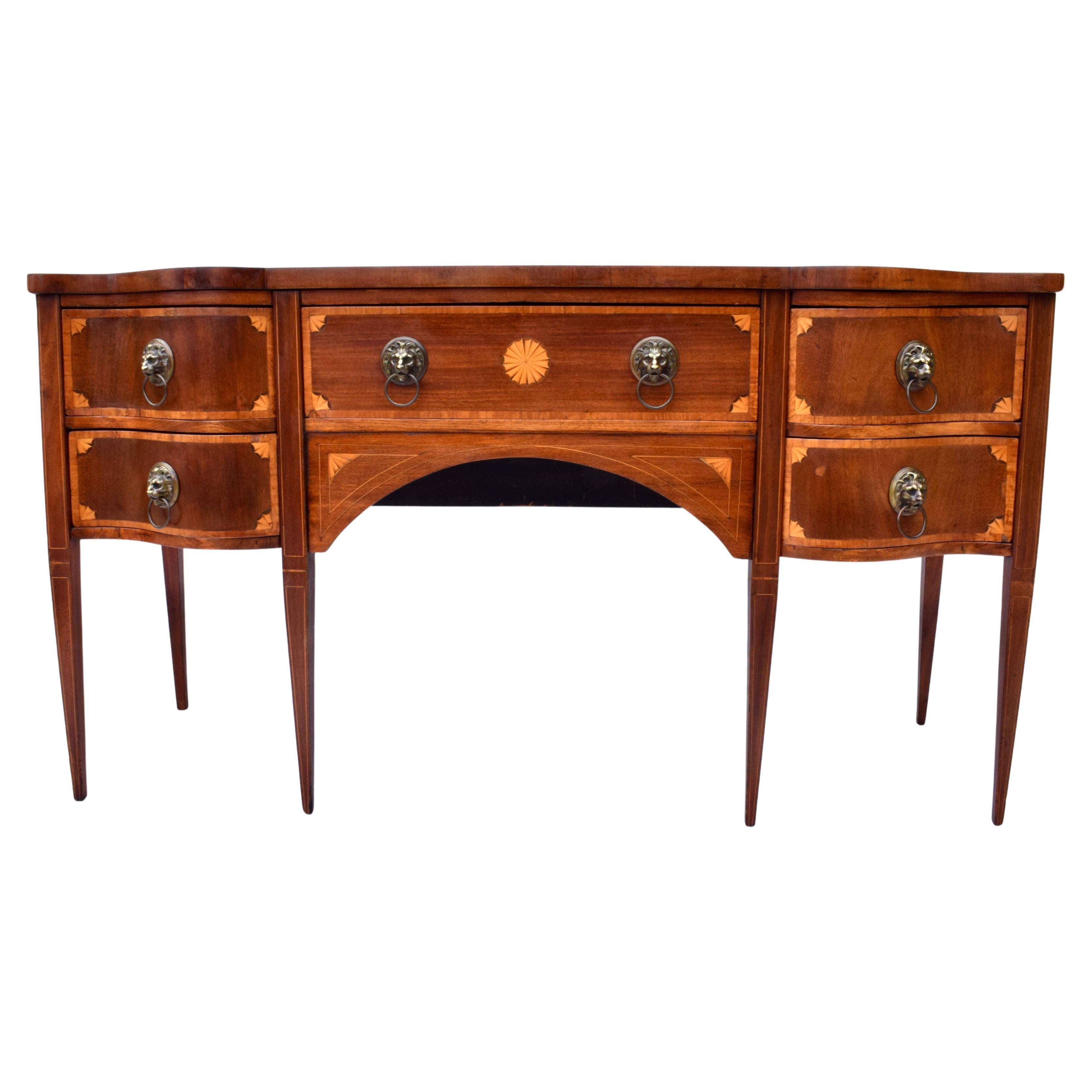 Fabulous early 20th century English style Sheraton or Hepplewhite Style Mahogany Serpentine Sideboard with superb figured form, handsome Satinwood inlay detailing and cast brass lion’s head pulls. Generous storage in the five dovetail drawers.