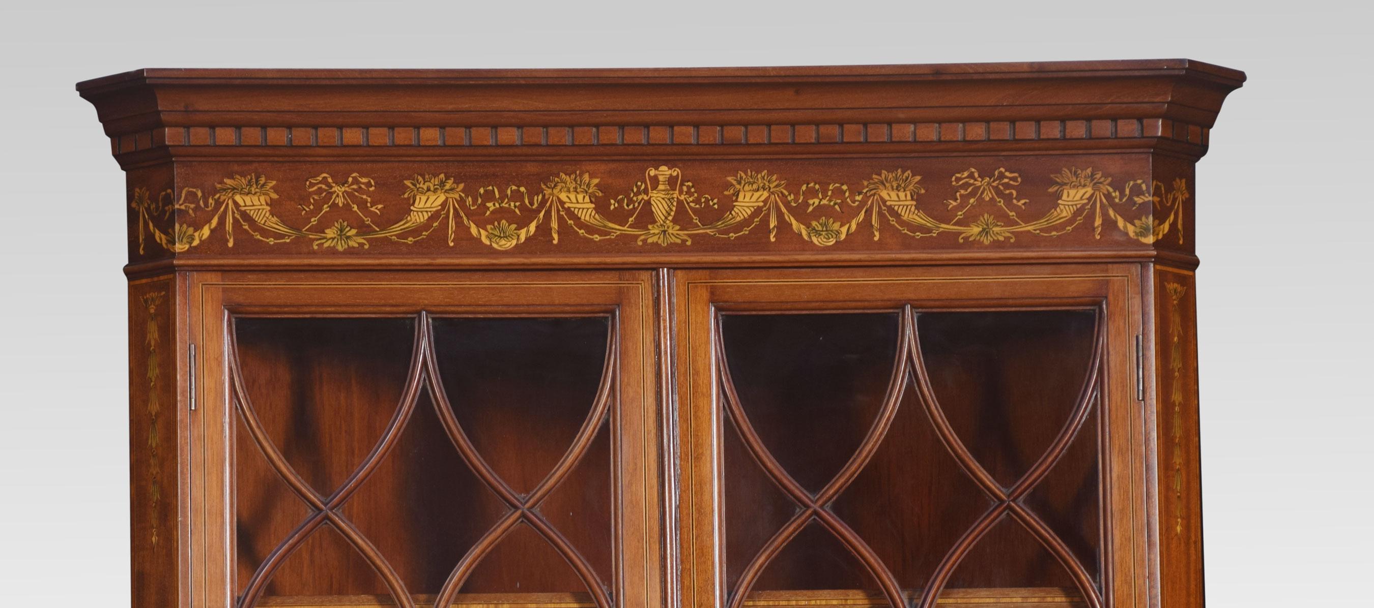 Eckschrank aus Mahagoni, Satinholz und Intarsien, mit geformtem Gesims über zwei verglasten Türen, die zwei feste Einlegeböden umschließen. Der untere Teil mit entsprechendem Fries und zwei Schranktüren, die kunstvoll mit Intarsien verziert sind,
