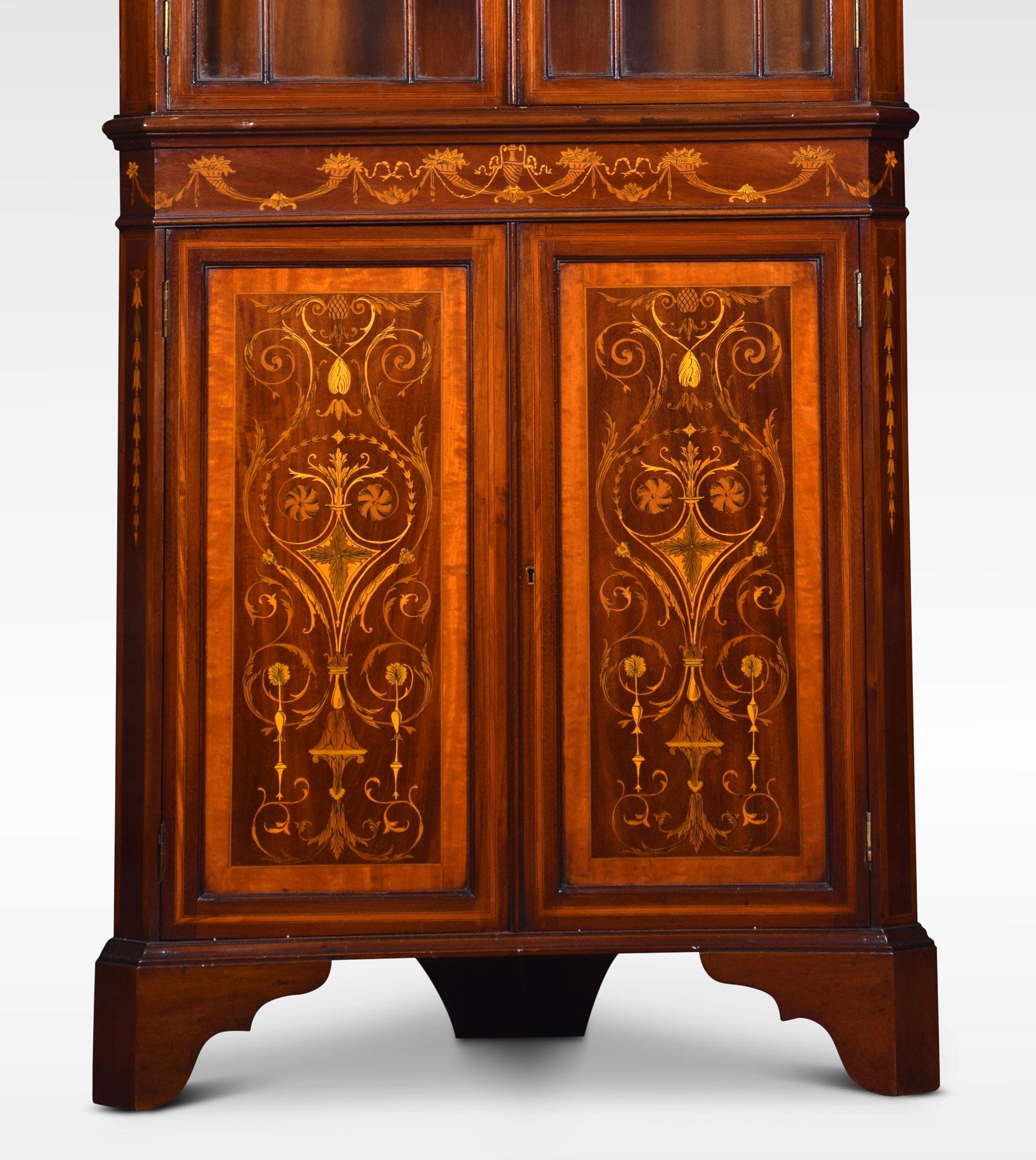 Mahogany, satinwood and marquetry inlaid corner cabinet, the architecturally moulded cornice above two glazed doors enclosing two fixed shelves. The lower section with conforming frieze and two cupboard doors elaborately decorated with marquetry