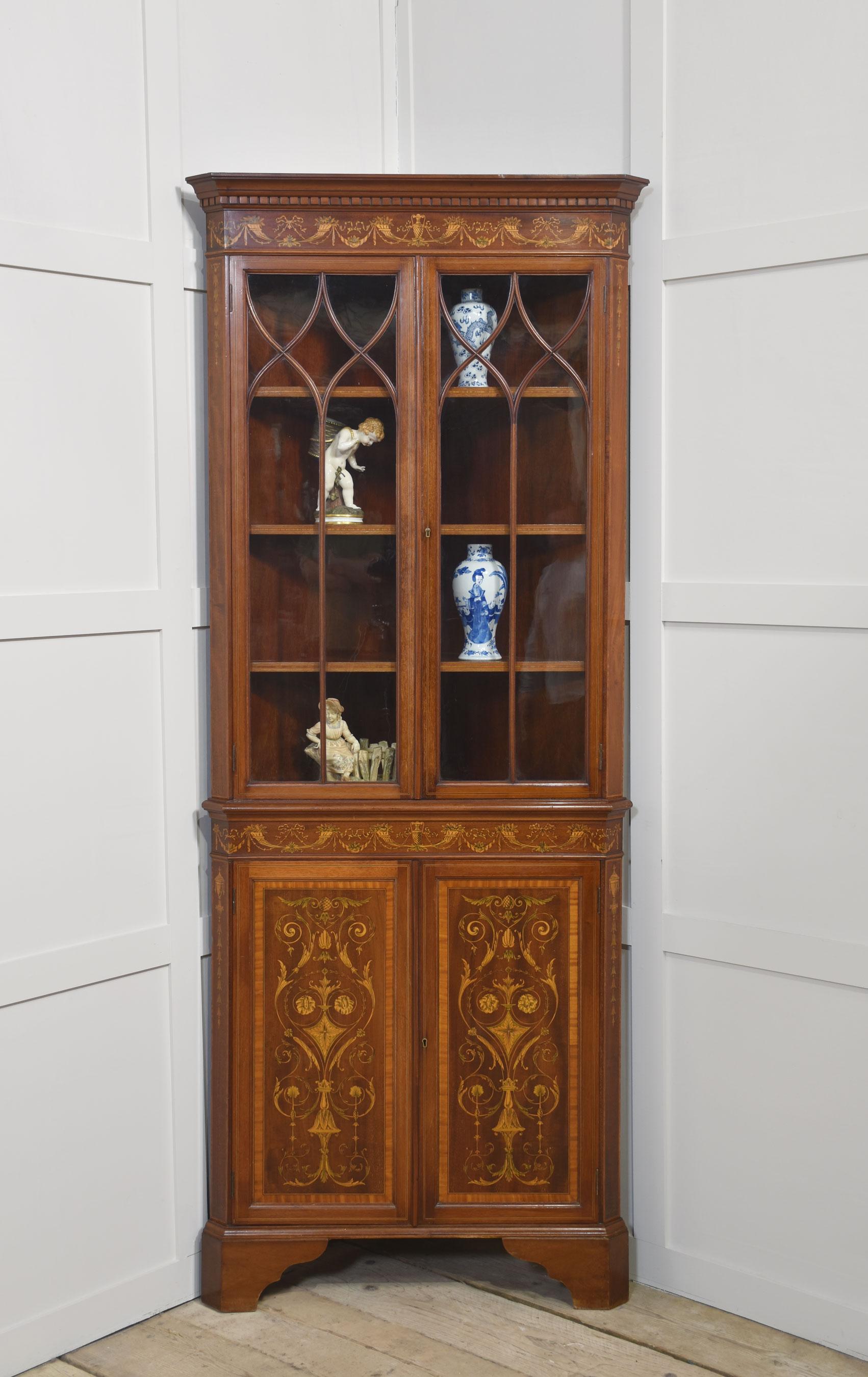 Mahogany, satinwood, and marquetry inlaid corner cabinet, featuring a moulded cornice above two glazed doors enclosing two fixed shelves. The lower section with a conforming frieze and two cupboard doors elaborately decorated with marquetry panels