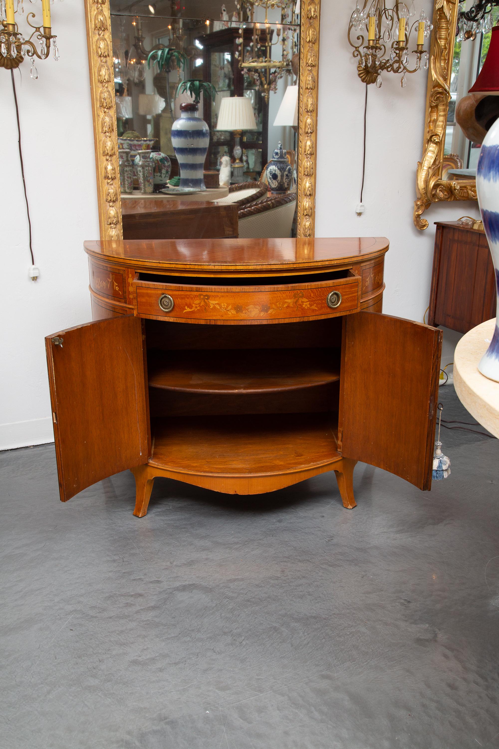 This is a lovely English Adams style mahogany bow front chest with satinwood inlay. The wood top is over a large inlaid drawer about two inlaid cabinet doors. The case piece is raised on splay feet, 20th century.