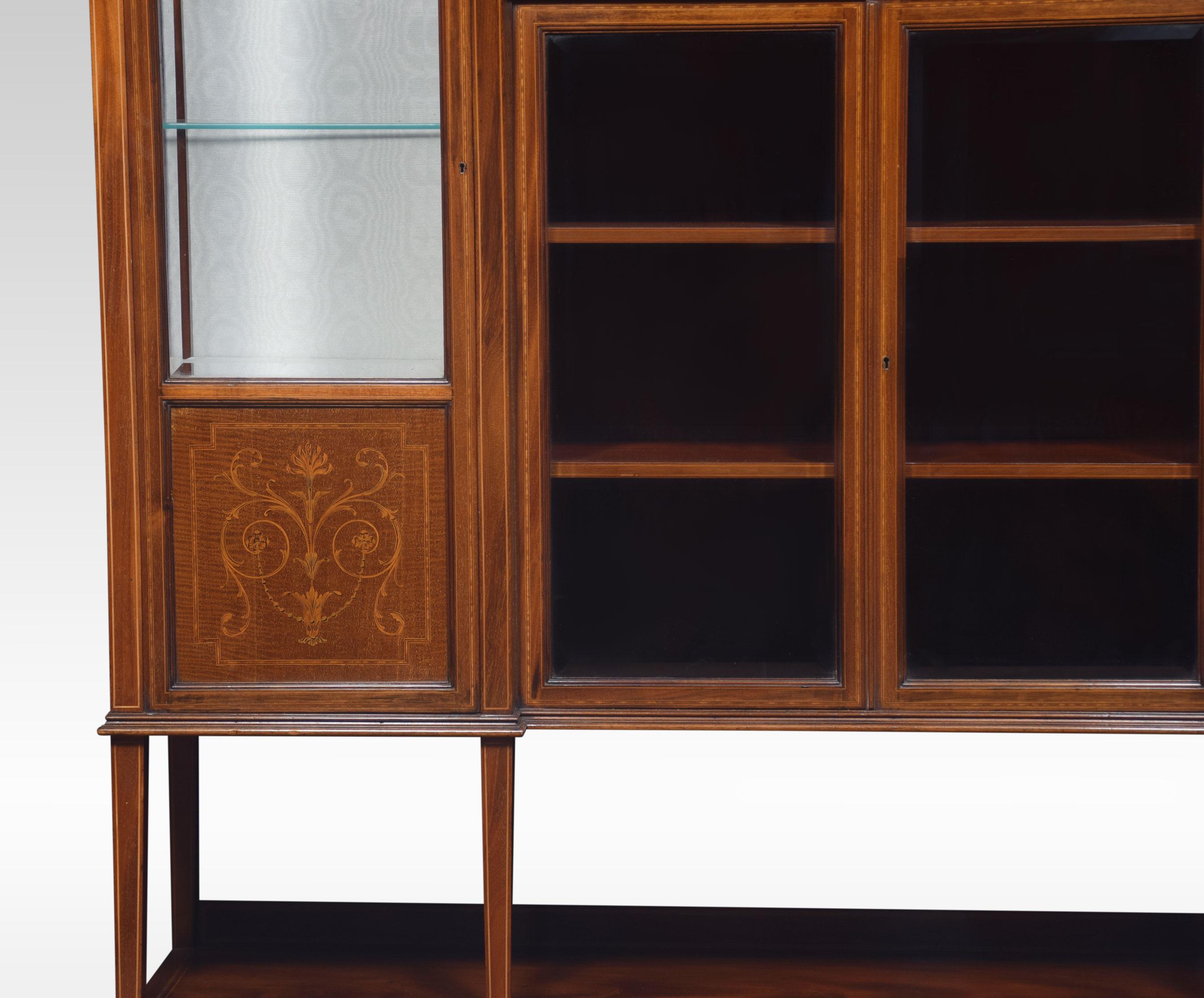 Mahogany inlaid inverted breakfront display cabinet, the molded top to the central beveled mirror back arcaded recess above three small drawers, and a pair of glazed doors below flanked by a pair of glazed cabinet doors enclosing a lined interior