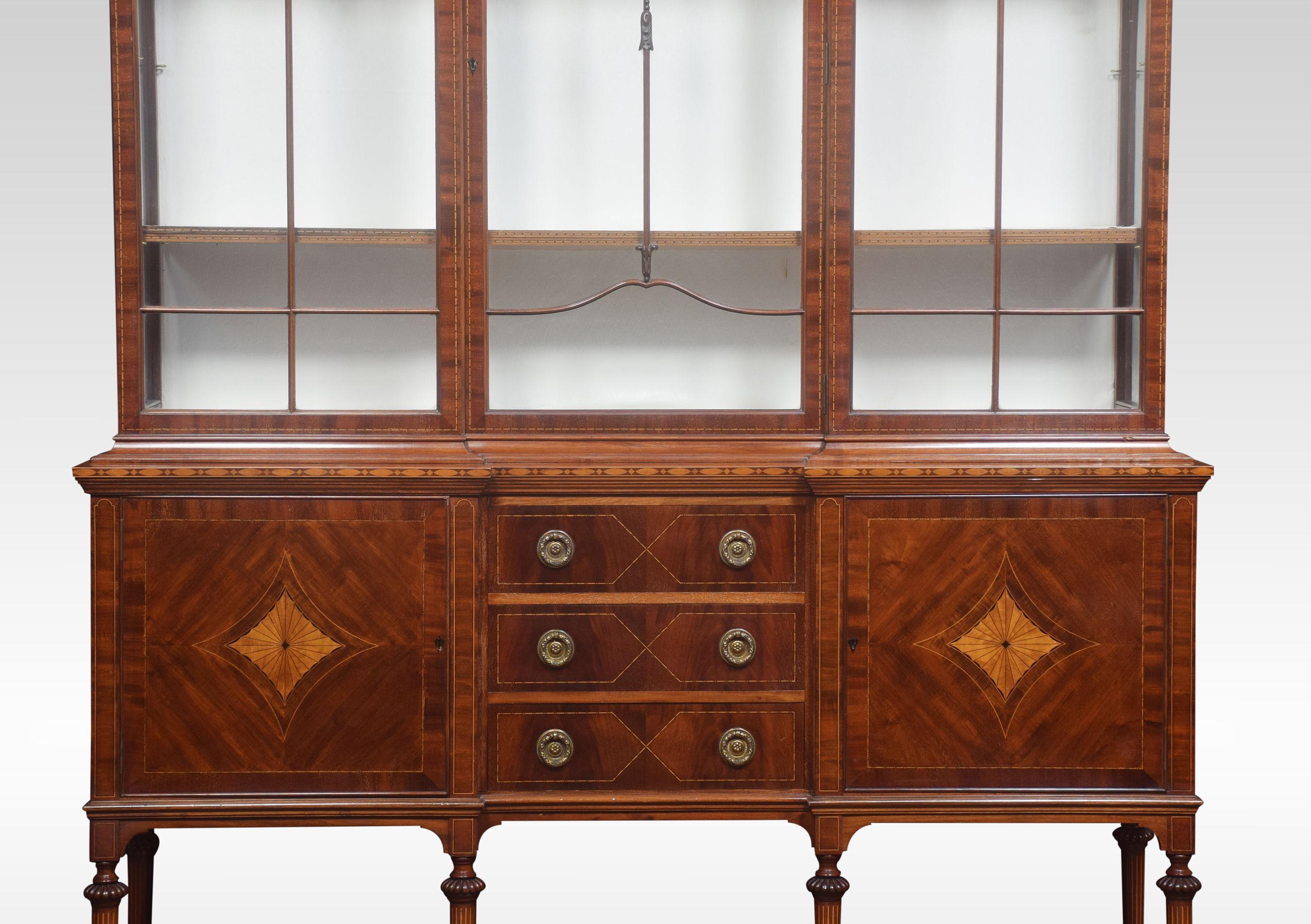 Mahogany display cabinet with double dome top above central single-segmented glass door flanked by glazed sides. The central door opening to reveal shelved upholstered interior. The base section fitted with three central inlaid drawers with brass