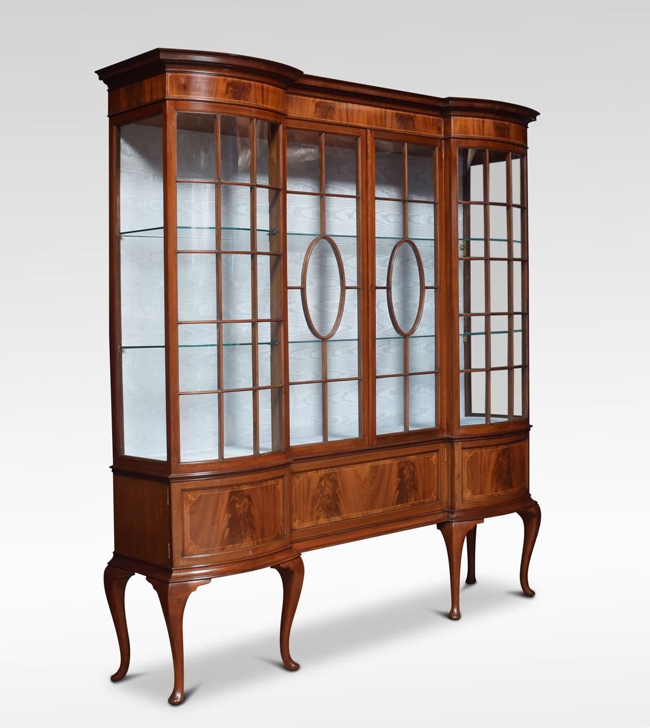Mahogany display cabinet, having shaped top over string inlaid panel above a two glazed centre doors section flanked by bowed ends. Enclosing two glass shelves and watermark silk lined interior the base section fitted with three panelled and inlaid