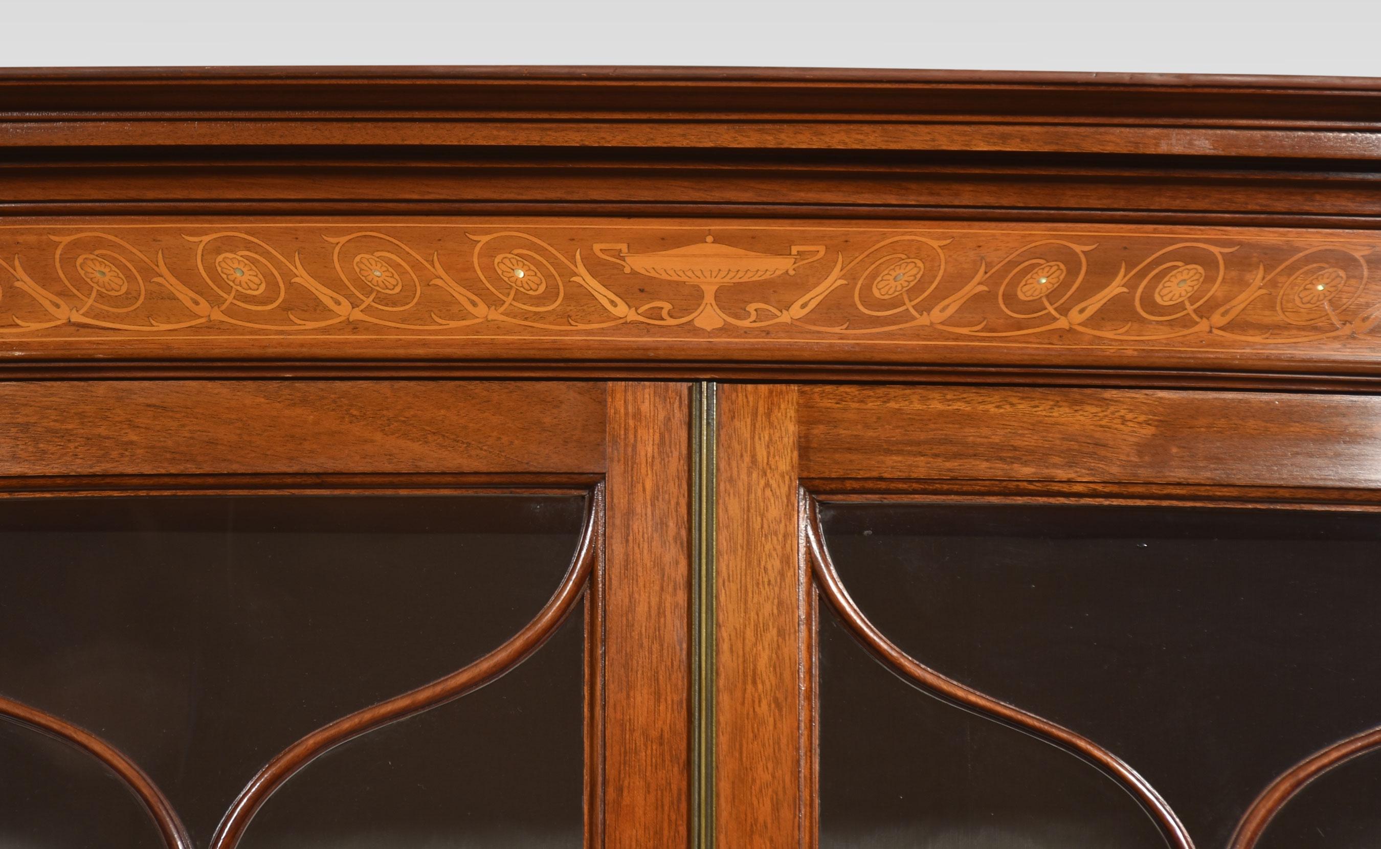 Mahogany bow front display cabinet. Having a moulded cornice above a pair of glazed centre doors enclosing shelved and watermark silk upholstered interior, flanked by glazed ends, with four inlaid cupboard doors below. All raised up on fluted