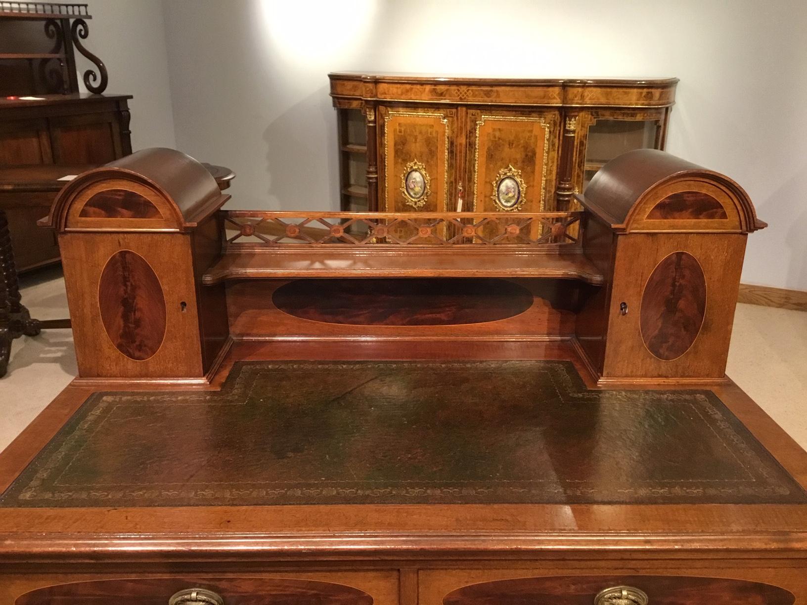 A mahogany inlaid Edwardian period ladies writing table. The upper section having a fretwork gallery, shaped shelf and domed end cabinets, enclosing letter racks, pen trays and ink well compartments. The lower section with a green leather writing