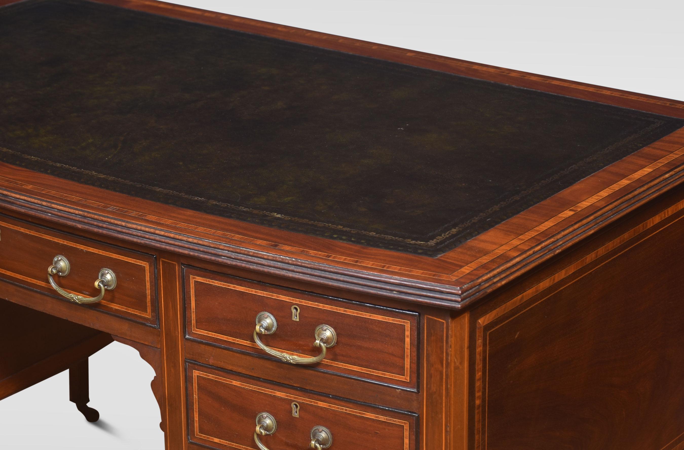 Mahogany inlaid desk. The top with inset green leather surrounded by a mahogany inlaid border. Above an arrangement of drawers with similar inlaid decoration and brass handles. Raised on tapered supports terminating in brass