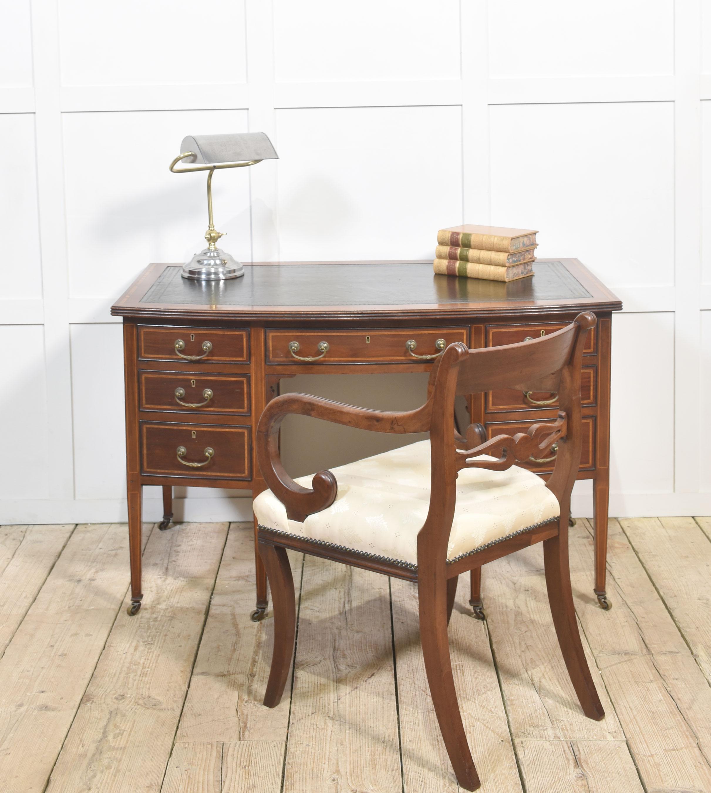Mahogany inlaid desk. The top with inset green leather surrounded by a mahogany inlaid border. Above an arrangement of drawers with similar inlaid decoration and brass handles. Raised on tapered supports terminating in brass