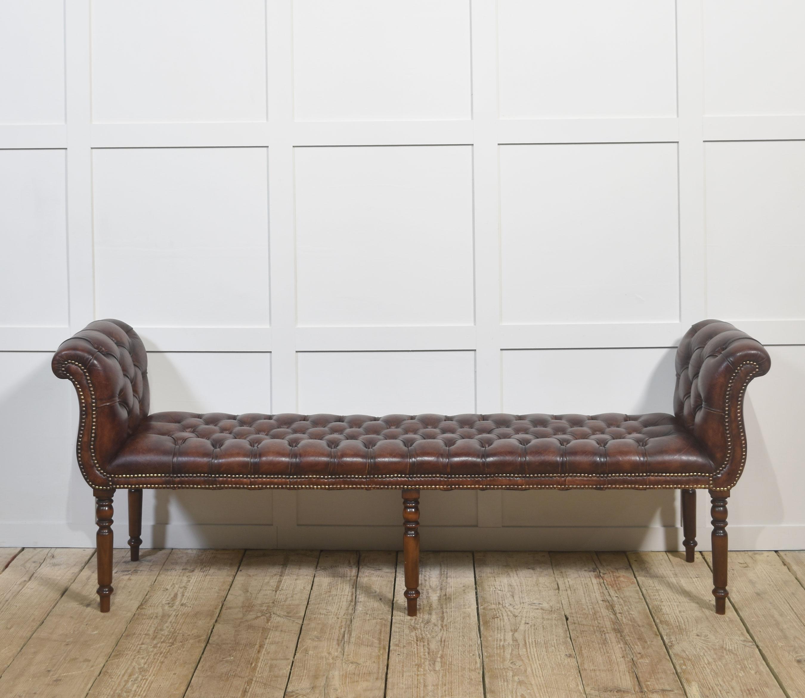 A timeless expression of English craftsmanship, this bench is upholstered in hand-finished brown leather with deep button tufting and elegant scroll ends. Antique brass stud detailing and turned solid wood legs complete the classic silhouette.