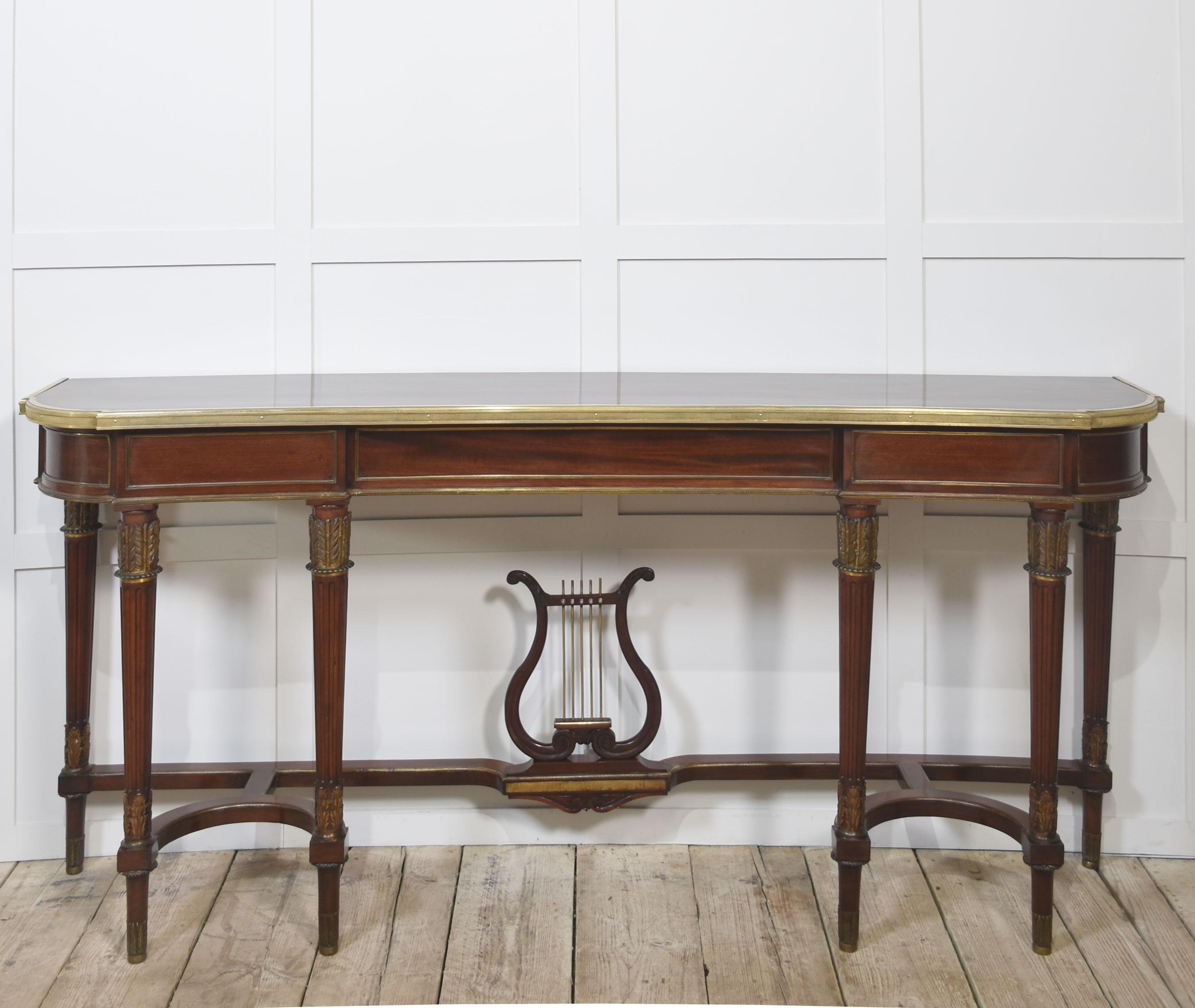 Longue table console en acajou, le plateau en acajou bien structuré bordé de laiton, reposant sur une frise moulurée et soutenu par six pieds fuselés et cannelés avec des montures en laiton. Les pieds sont reliés entre eux par des brancards