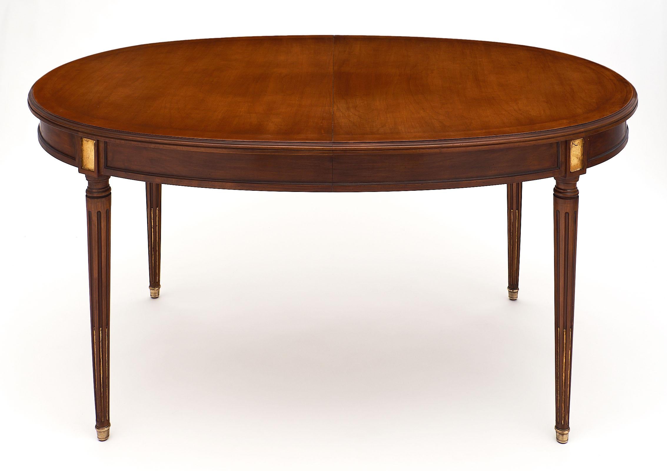 Louis XVI style antique mahogany dining table featuring an oval shape and gold leaf detail. We love the long, tapered legs and bronze feet. This table has been finished with a natural wax. The table does open for additional leaves, though we do not