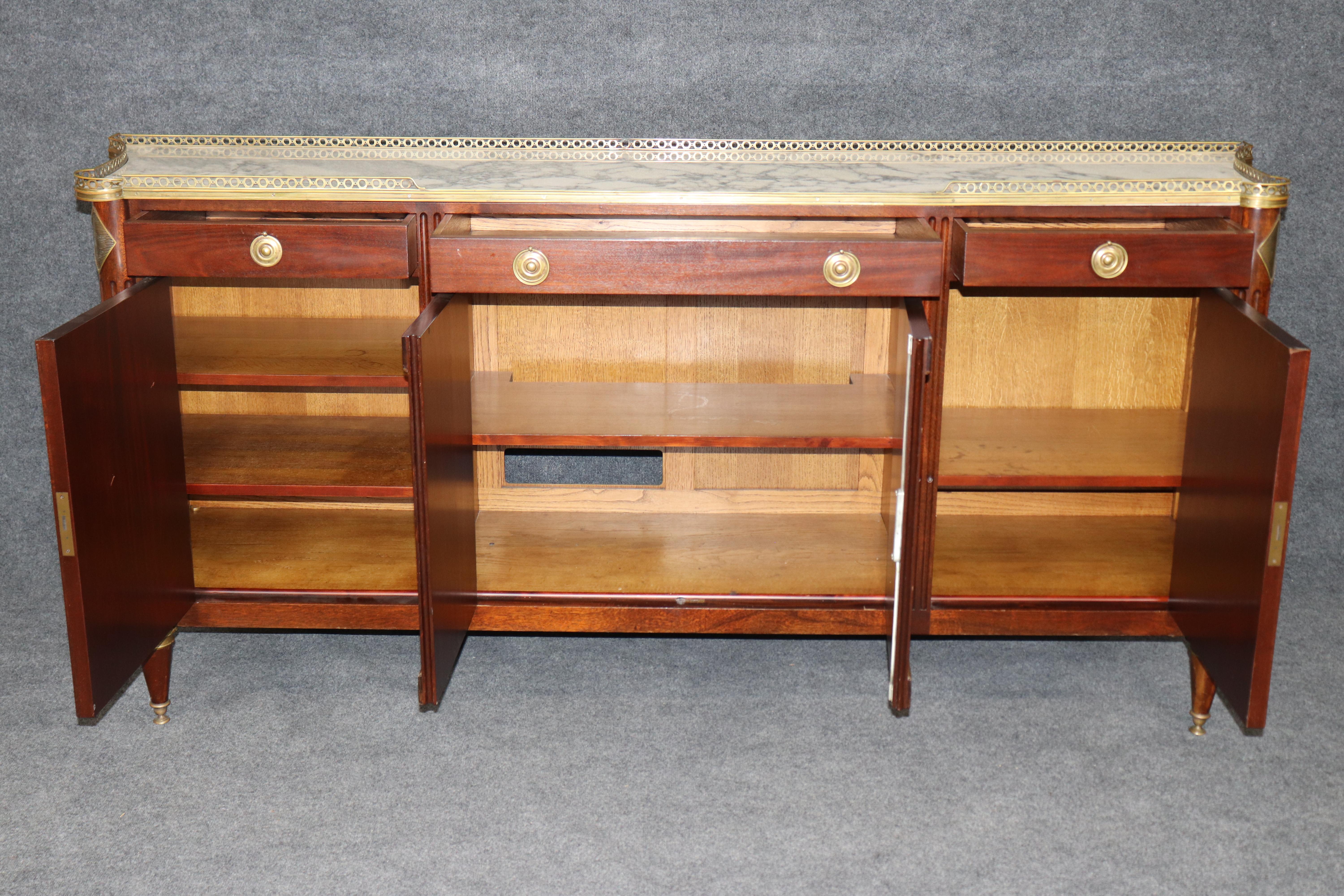 Eleganza per i tuoi interni con questa credenza francese degli anni '40 con piano in marmo montato in bronzo, un mix sorprendente di funzionalità ed eleganza raffinata. Questa credenza vintage presenta un'imponente struttura in mogano ornata da
