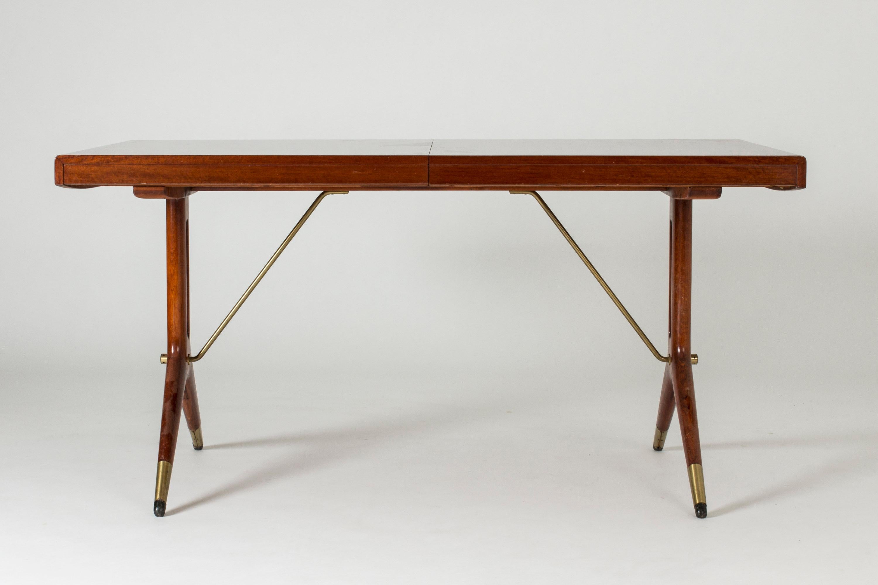 Beautiful mahogany dining table by David Rosén for Nordiska Kompaniet. Y-shaped legs and brass rods balancing the table give it an elegant and unique Silhouette. Two inlays measuring 45 cm each.
