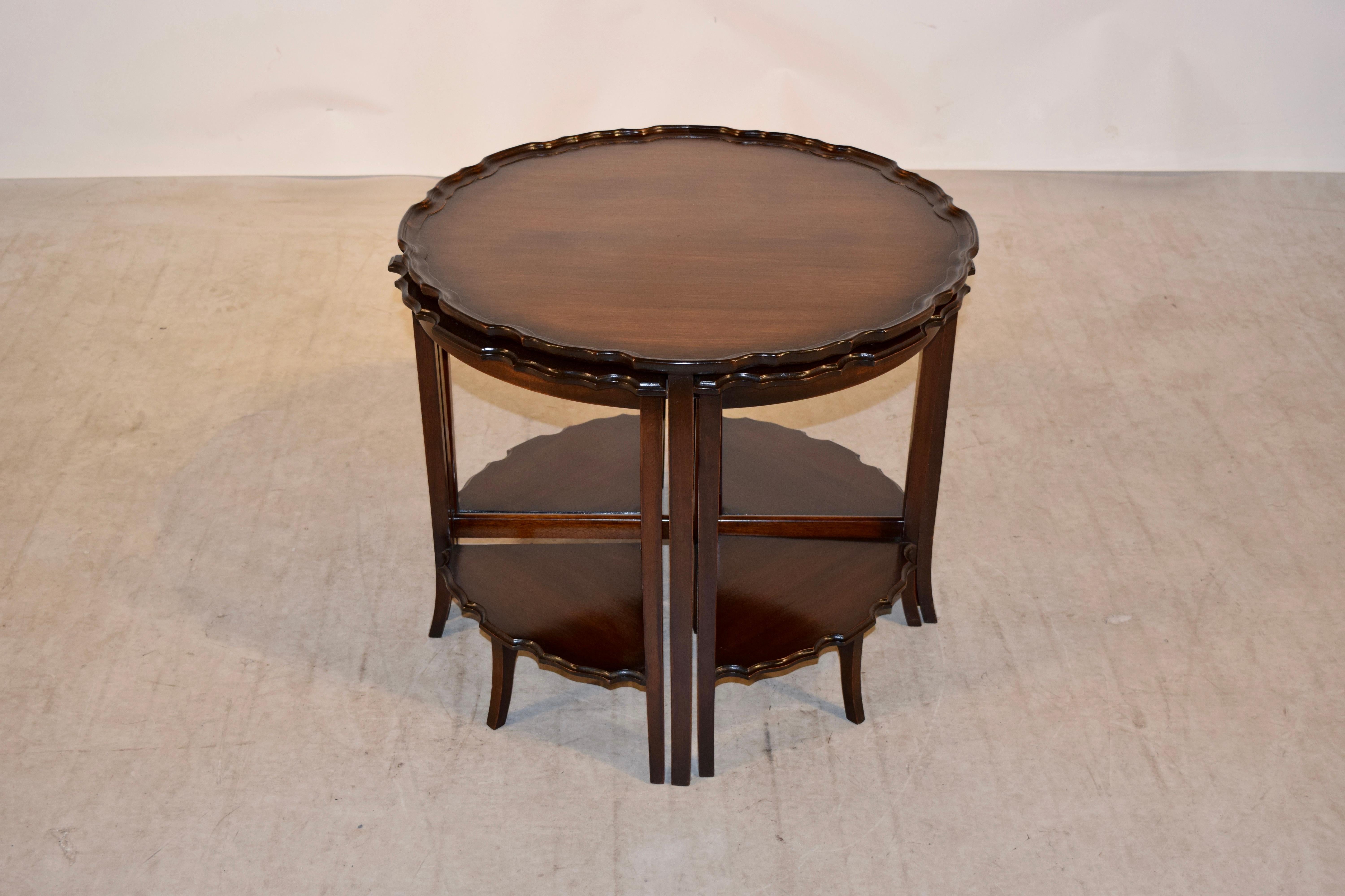 Mahogany nest of tables from England. The top of the central table has a molded pie crust edge, and is supported on four legs with splayed feet joined by cross stretchers. There are four additional small tables which nest underneath that have the