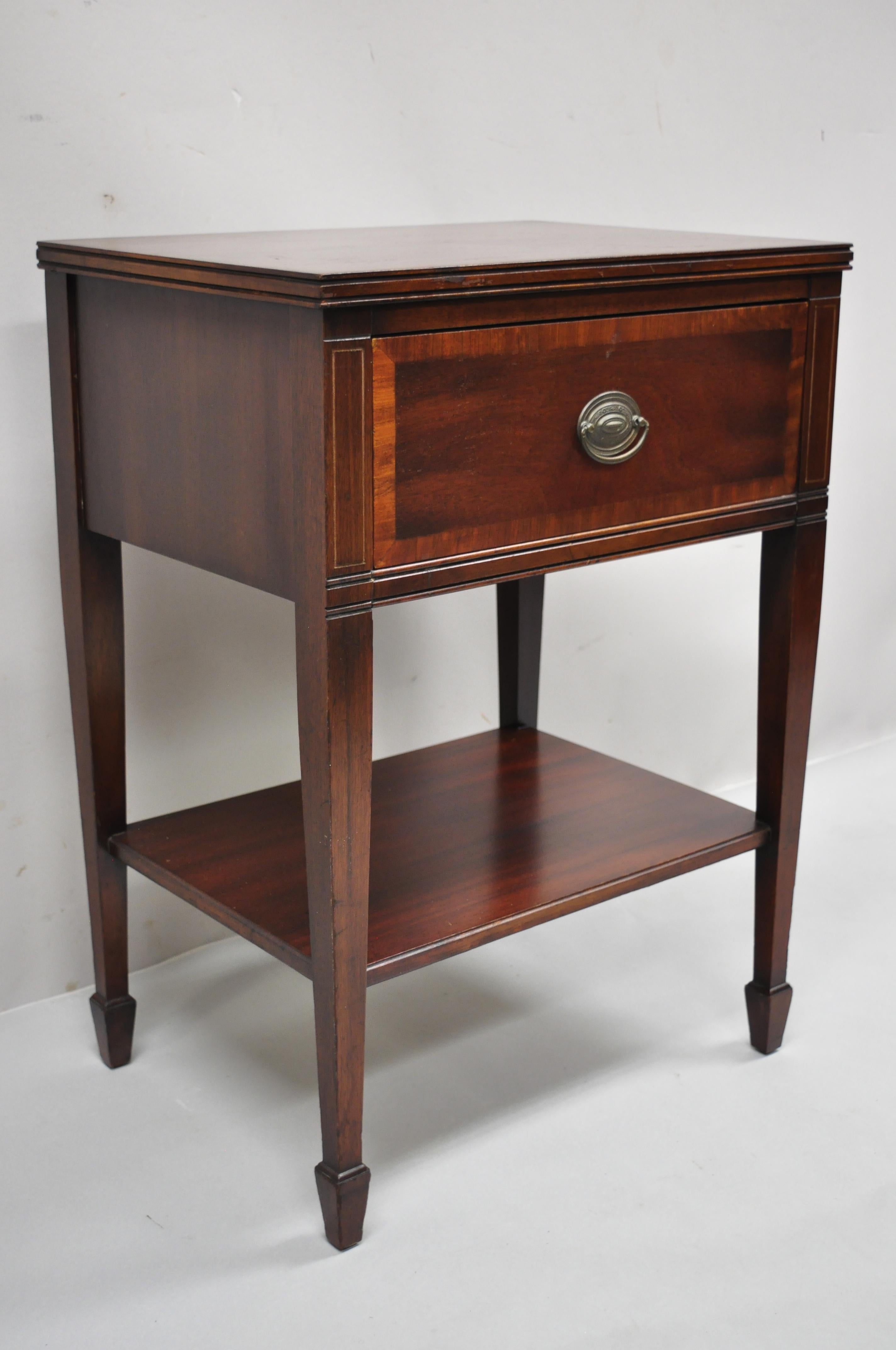 Mahogany one drawer banded inlay Sheraton federal nightstand bedside table by Stiehl. Item features banded drawer front, lower shelf, beautiful wood grain, tapered legs, solid brass hardware, quality American craftsmanship. Circa Early 1900s.