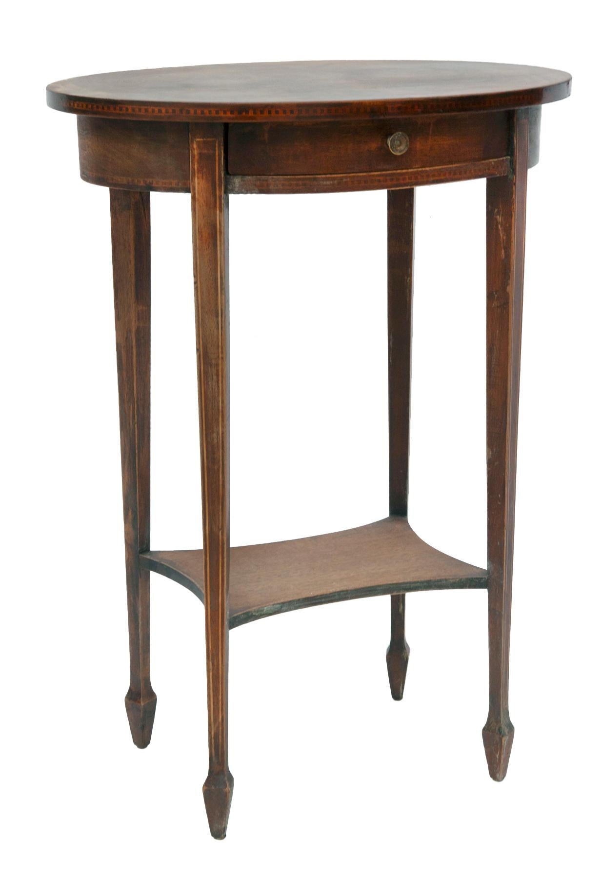 Slender pair of early 20th century oval mahogany tall side tables with a single drawer. The tables have a lower tier shelf.