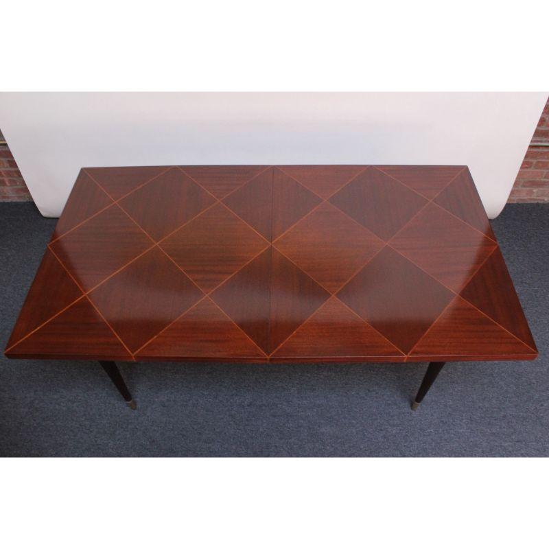 Exquisite dining table with two additional leaves designed by Tommi Parzinger in the early 1950s for Charak (USA).
Parquetry surface is adorned with a diamond pattern in mahogany with a satinwood border. Ebonized, tapered, fluted legs are supported