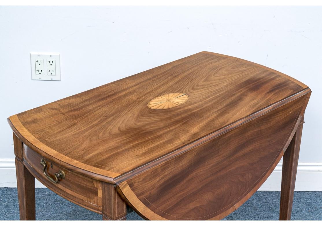 Para restauración. Mesa Pembroke de caoba con bandas de madera satinada y medallón central de concha incrustado. 
Sobre patas cónicas cuadradas con bandas, punteras y ruedas de latón. 

Estado: Requiere restauración, ver fotos detalladas. Gran