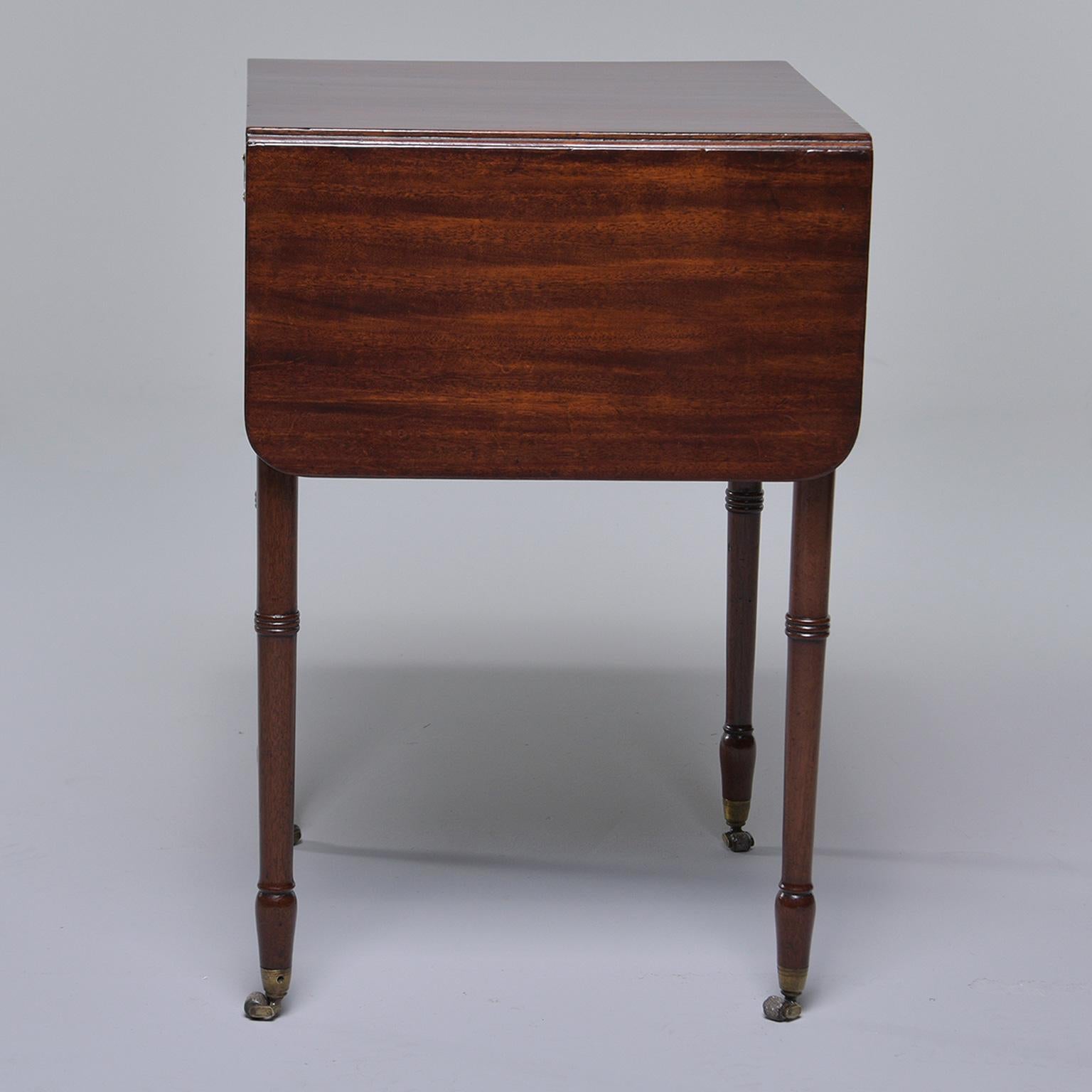 English mahogany Pembroke style table features turned legs and original brass casters hardware, circa 1900s. There is a functioning drawer on one side and a faux drawer with drawer front and hardware on the other. Unknown maker. 

Width shown is