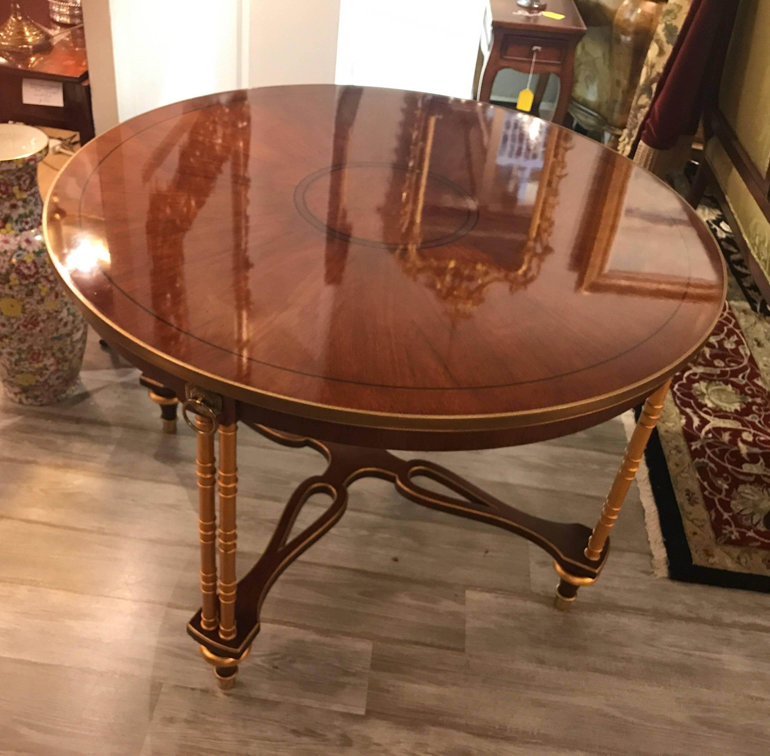 Elegant and graceful large Regency style mahogany and gilt centre table by Baker Furniture. The mirror smooth finished top with perfectly matched mahogany top and ebony inlay, supported by gilt legs and pierced snatcher base. A very hard to find