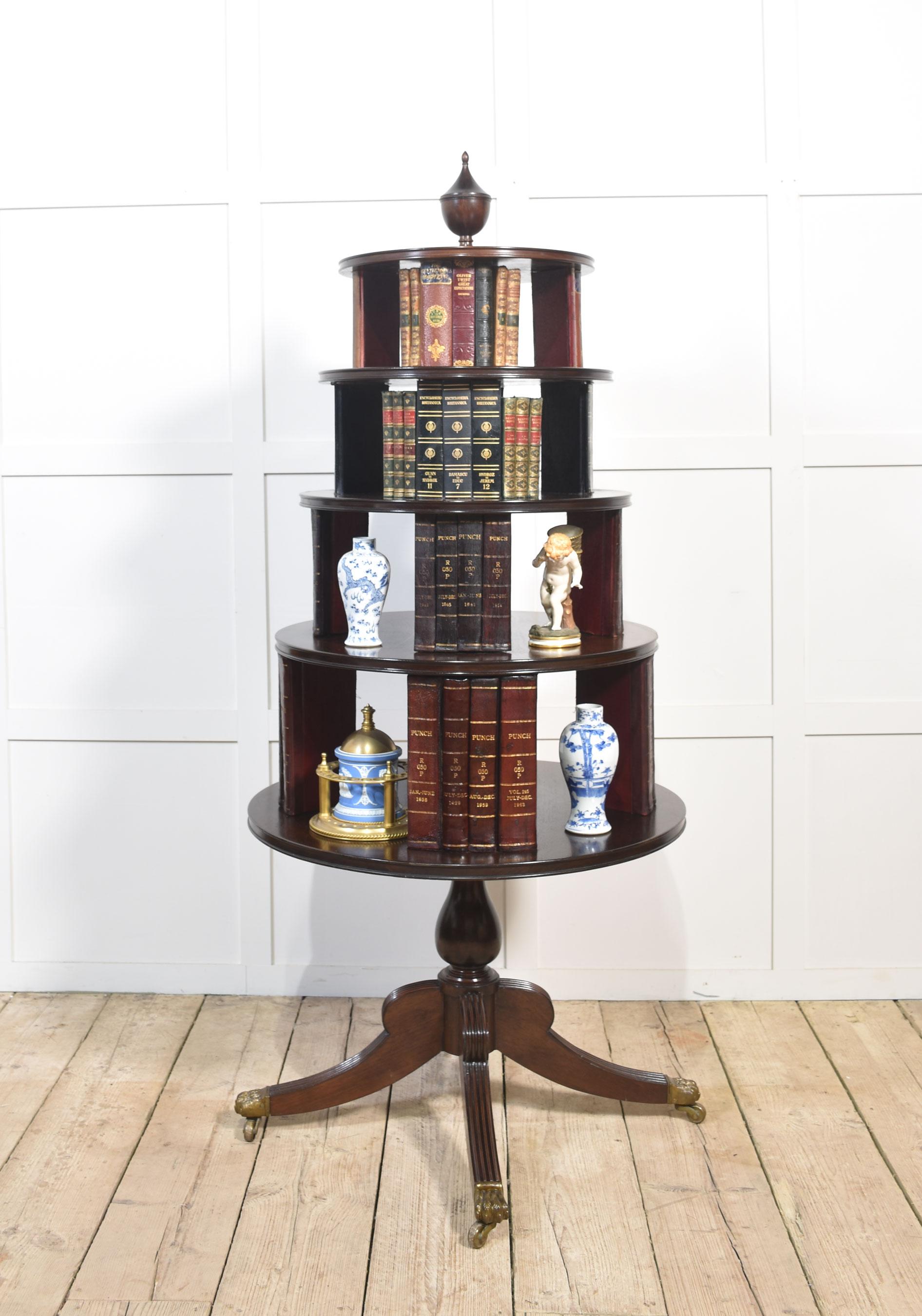 Libreria girevole in mogano in stile Regency, con terminale intagliato che sovrasta quattro piani circolari dotati di libri finti rilegati in pelle. Il tutto poggia su un gambo a bulbo e su quattro gambe strombate e ribattute. Termina con piedi a